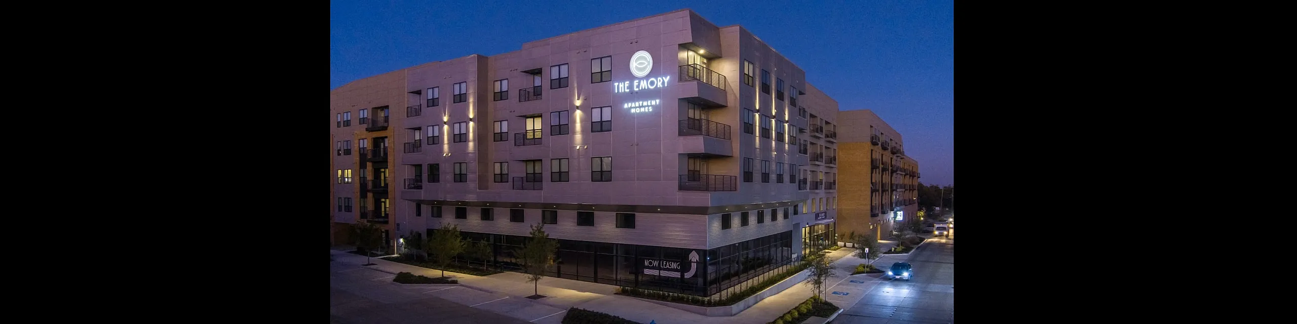 The Emory Apartment Homes building illuminated at dusk, showcasing modern architecture and inviting ambiance.