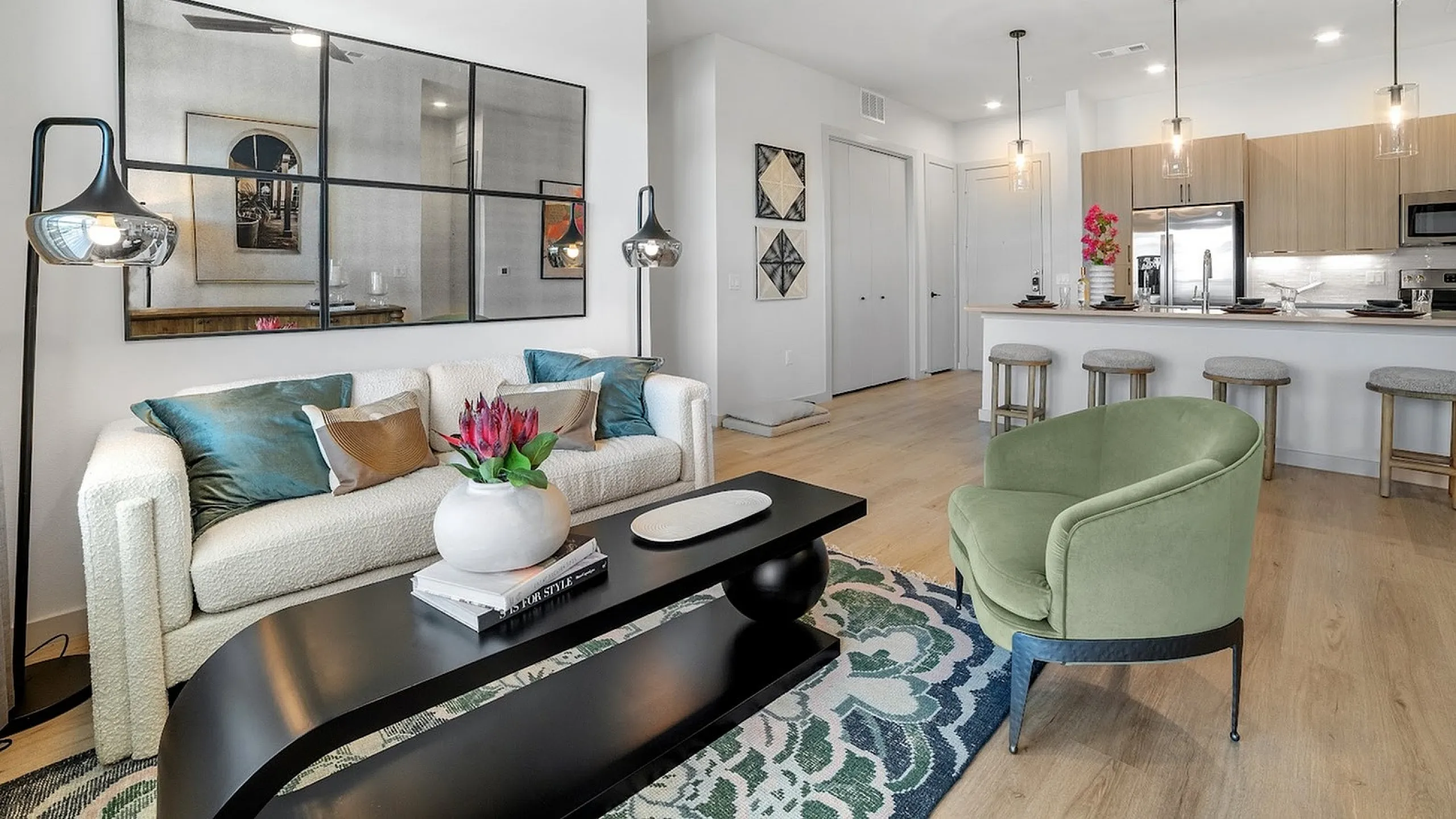 Contemporary apartment living room with elegant decor, featuring a cozy white sofa, chic green armchair, stylish black coffee table, and modern open kitchen with bar seating.