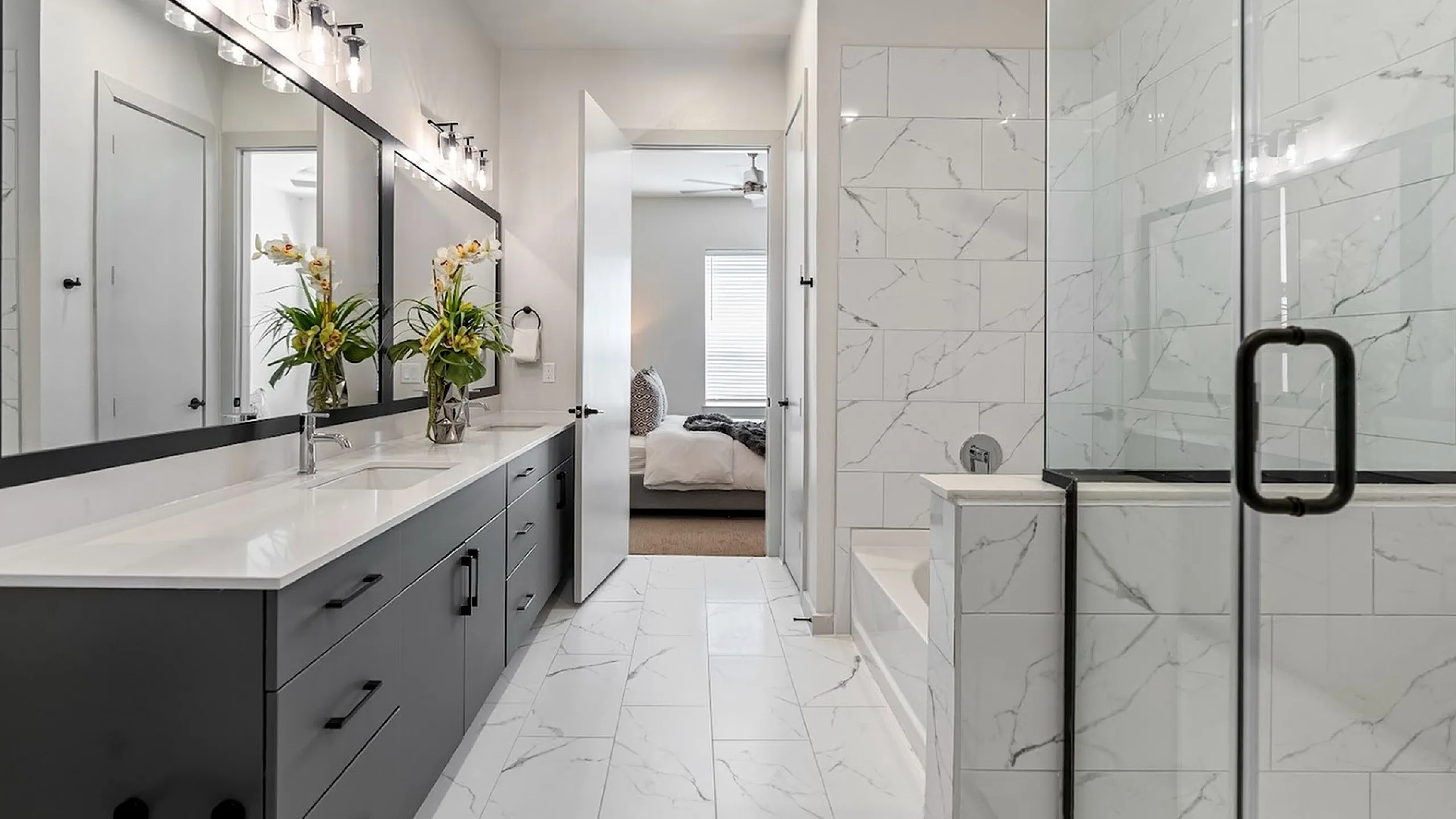 Luxurious modern bathroom featuring elegant marble tiles, a spacious glass shower, double vanity, and natural light flowing into an adjoining bedroom.