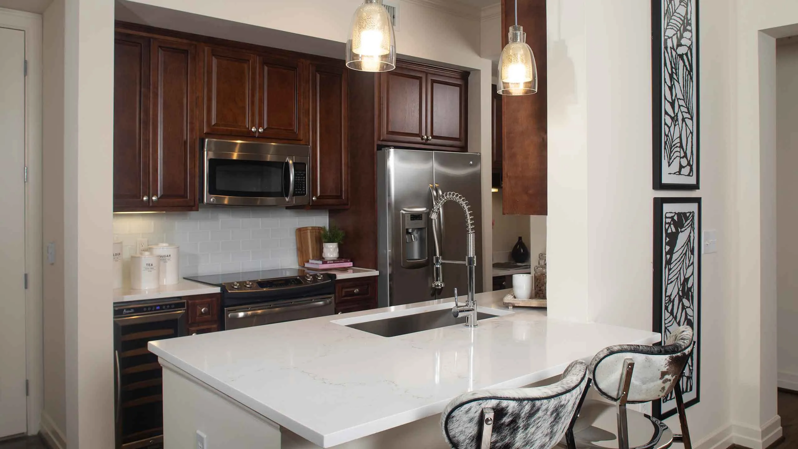 Modern kitchen with elegant dark wood cabinets, stainless steel appliances, and a sleek marble countertop illuminated by stylish pendant lights.