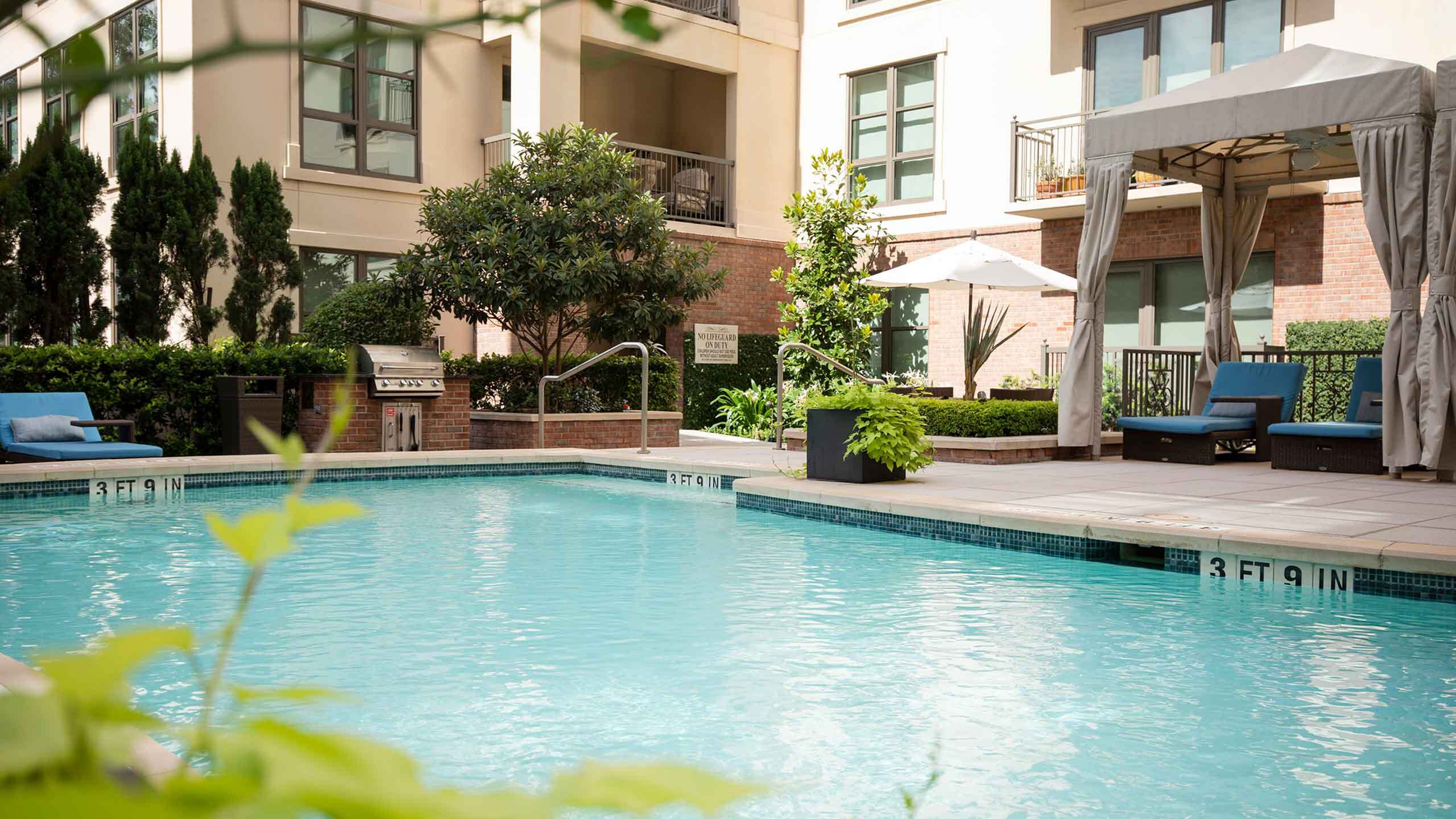 Inviting apartment swimming pool area featuring cozy lounge chairs, vibrant greenery, and modern outdoor amenities for relaxation and entertainment.