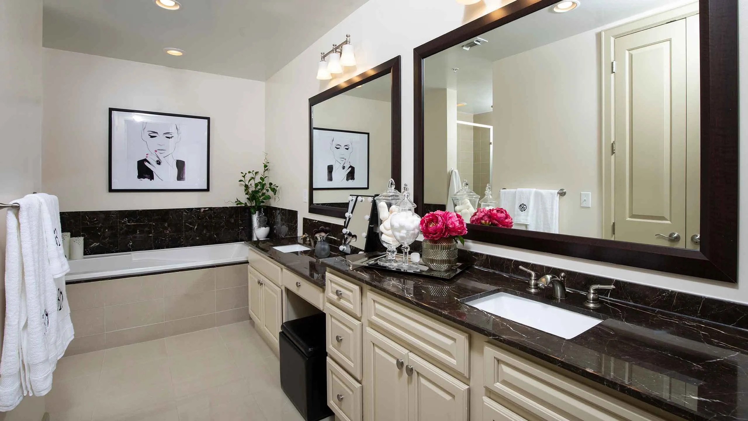 Luxurious bathroom featuring elegant dual sinks, polished black marble countertops, and stylish decor with floral accents.