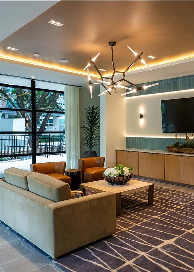 Modern apartment lounge with stylish lighting, contemporary furniture, and large windows overlooking greenery.