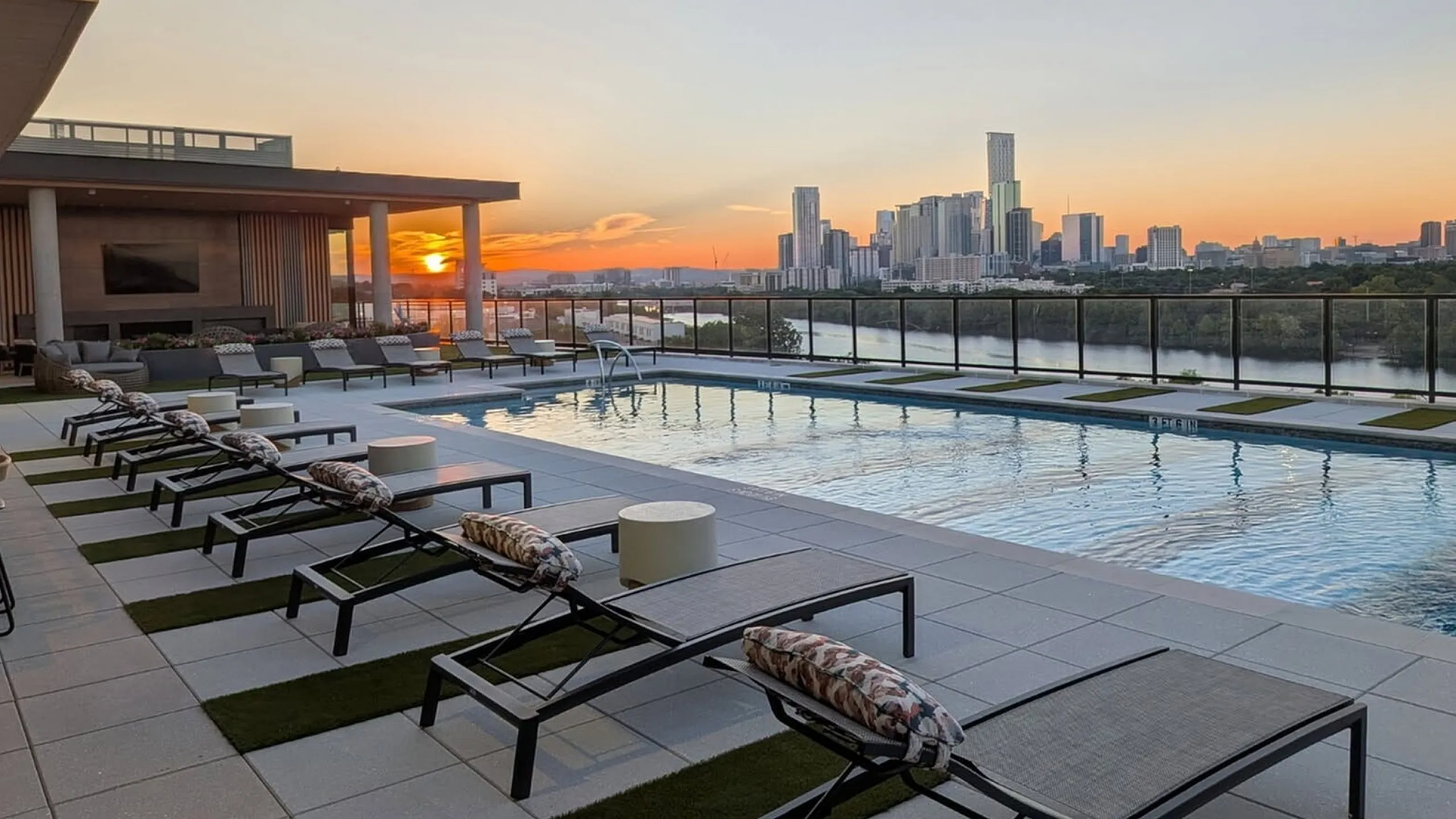 Luxurious rooftop pool with modern loungers and stunning city skyline at sunset.