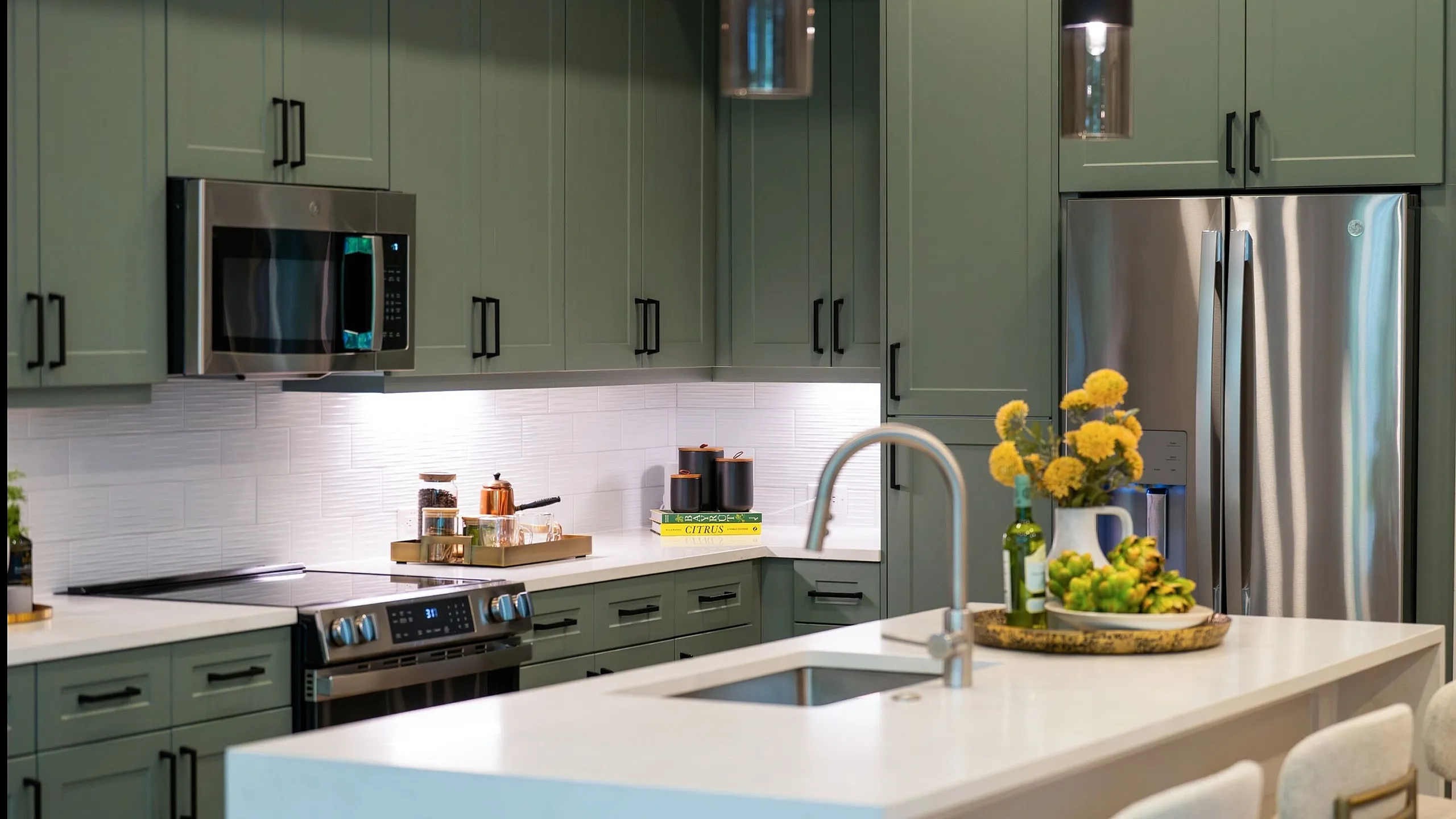 Modern kitchen with sleek green cabinetry, stainless steel appliances, and a stylish island featuring elegant seating and vibrant decor accents.