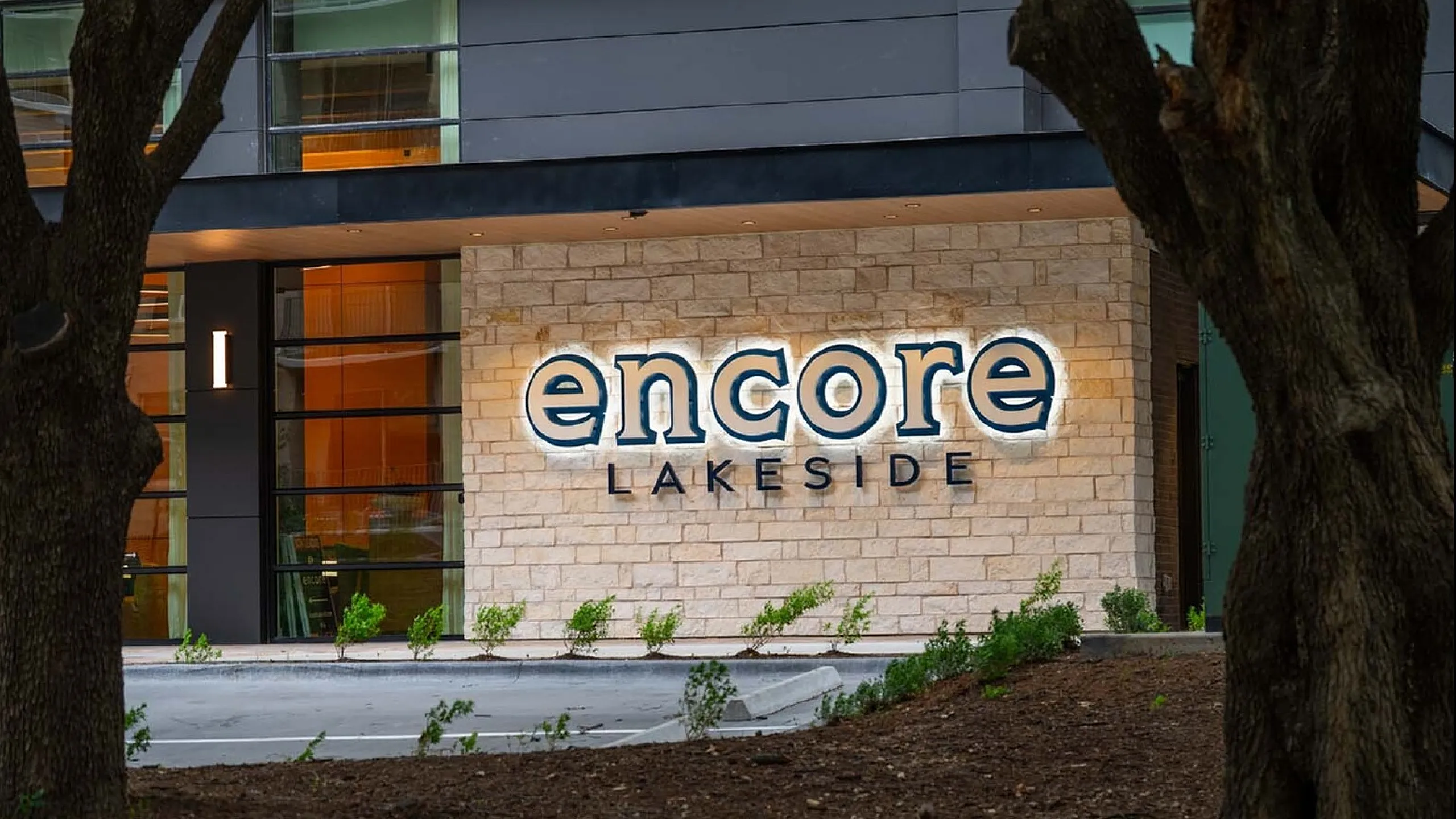 Modern apartment exterior with illuminated 'Encore Lakeside' sign, showcasing sleek architecture and stylish brickwork.