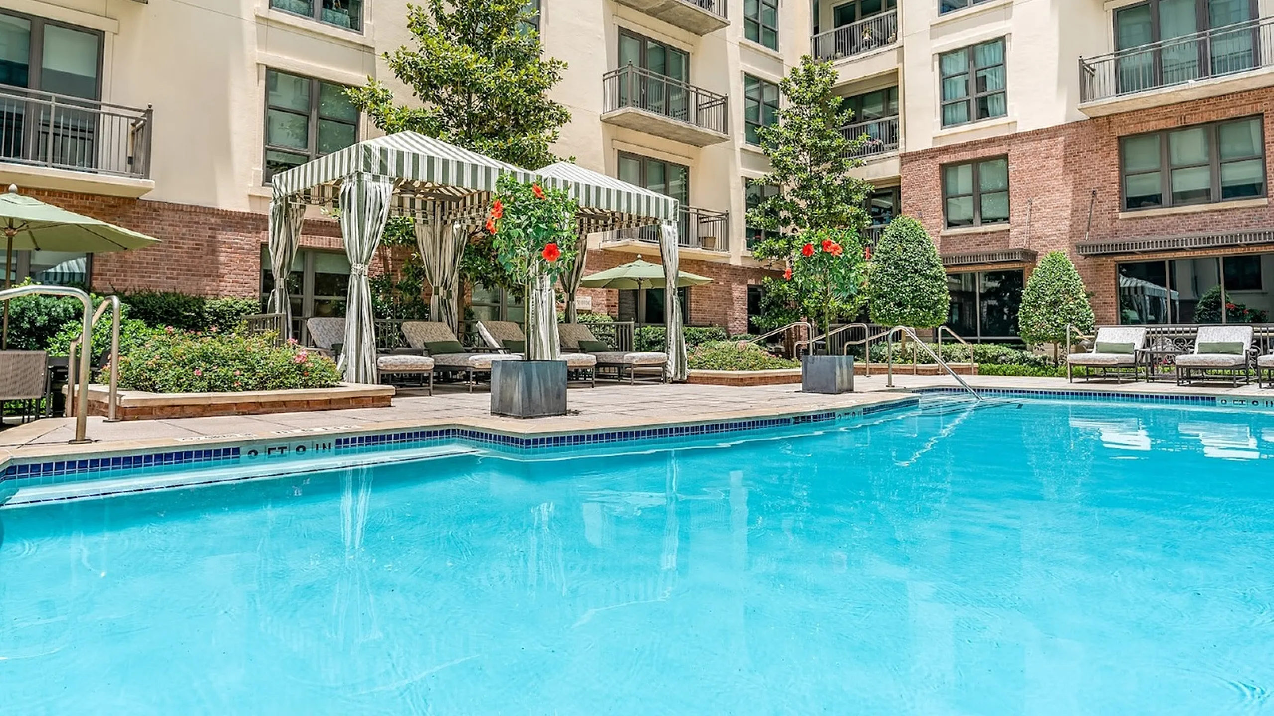 Inviting apartment swimming pool area featuring cozy lounge chairs, vibrant greenery, and modern outdoor amenities for relaxation and entertainment.
