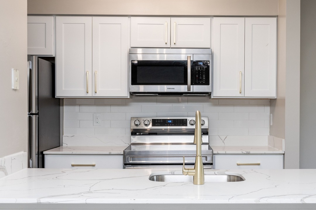 Modern Kitchen featuring marble style Quartz countertops and stainless steel appliances including microwave and pull down faucet in an Autumn Town Center apartment.