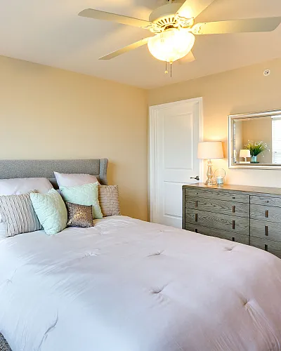 Elegant bedroom with a cozy queen-sized bed, soft pillows, and stylish wooden furniture under a bright ceiling fan.