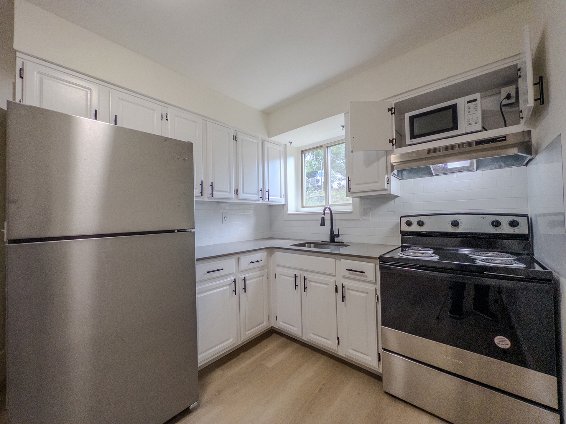 kitchen with white cabinets, stainless steel appliances, microwave, window over sink, stone countertops