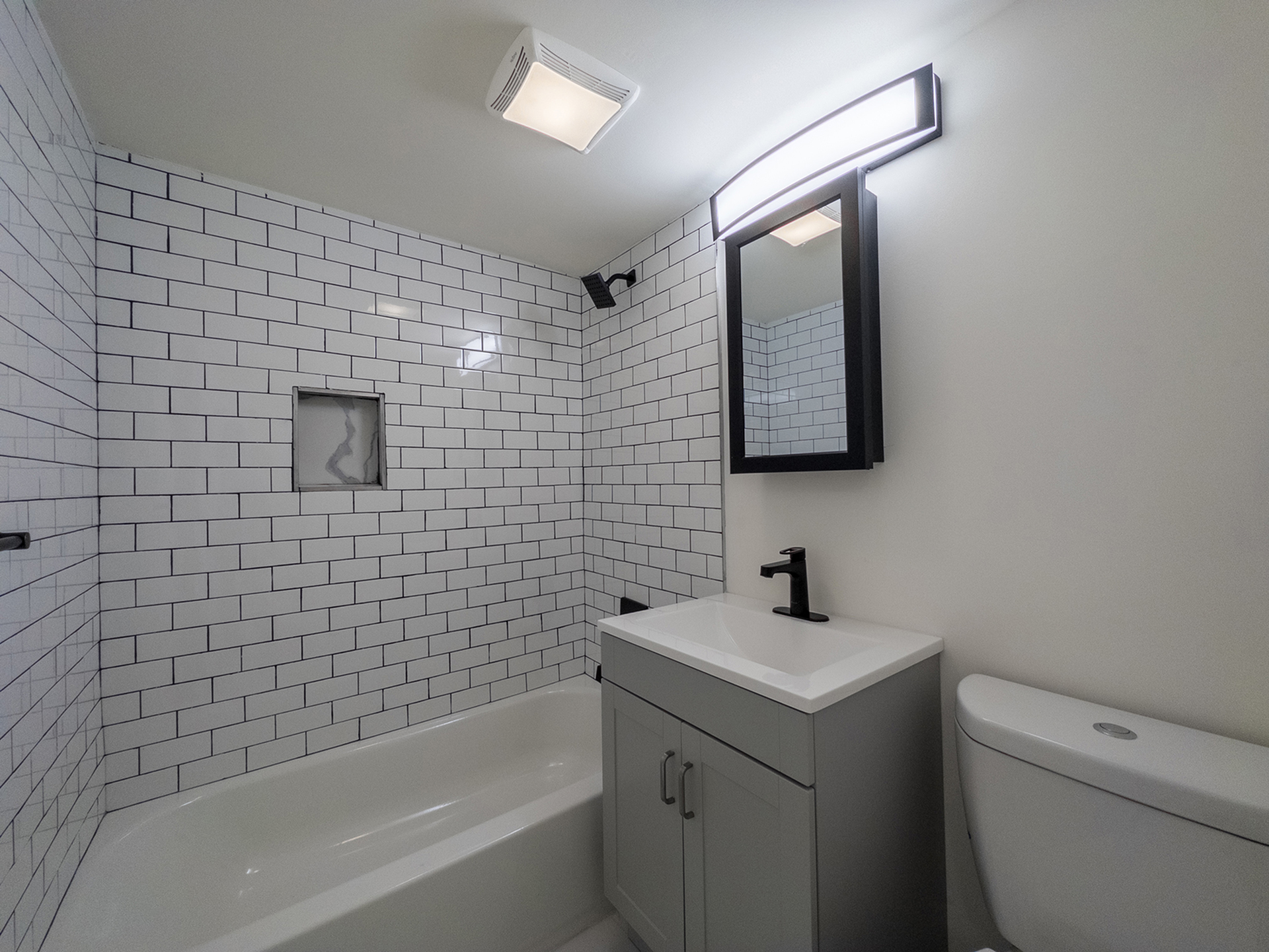 modern bathroom with subway tile shower including built in shelf, black accents, vanity sink