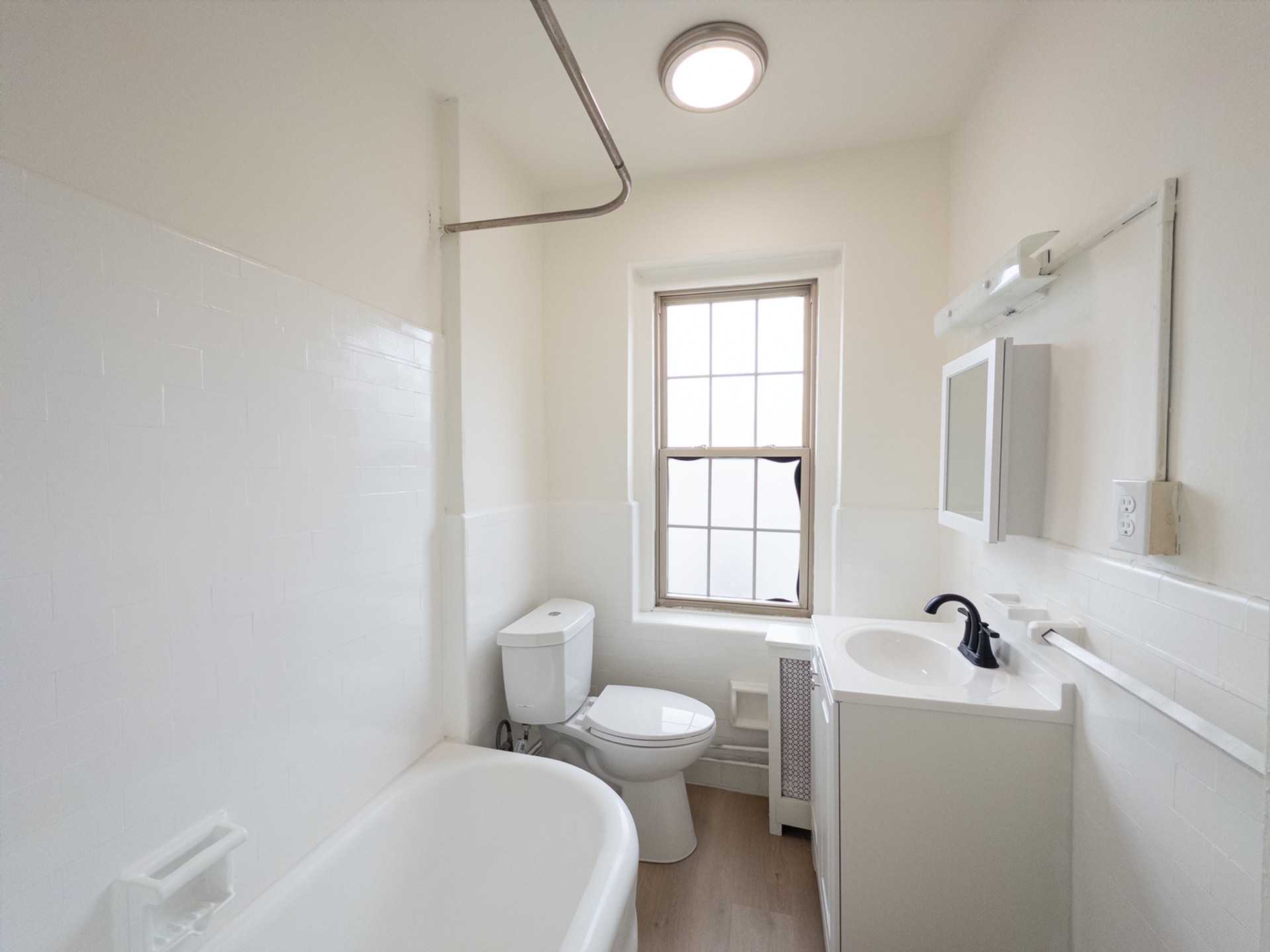 apartment bathroom, energy efficient toilet, vanity sink with medicine cabinet, overhead light, tub with shower head, big foggy window