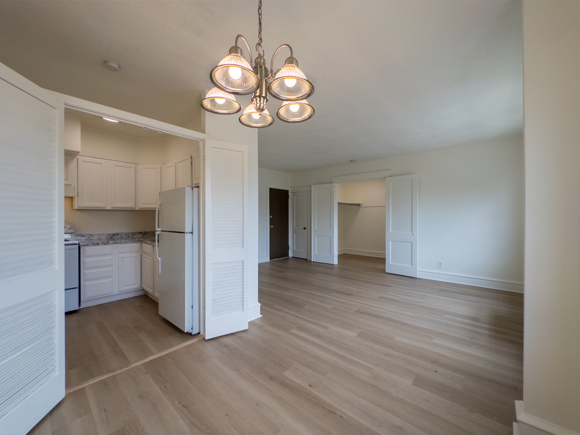 studio apartment, view from dining area with overhead light fixture, sliding doors leading to kitchen, wood floors