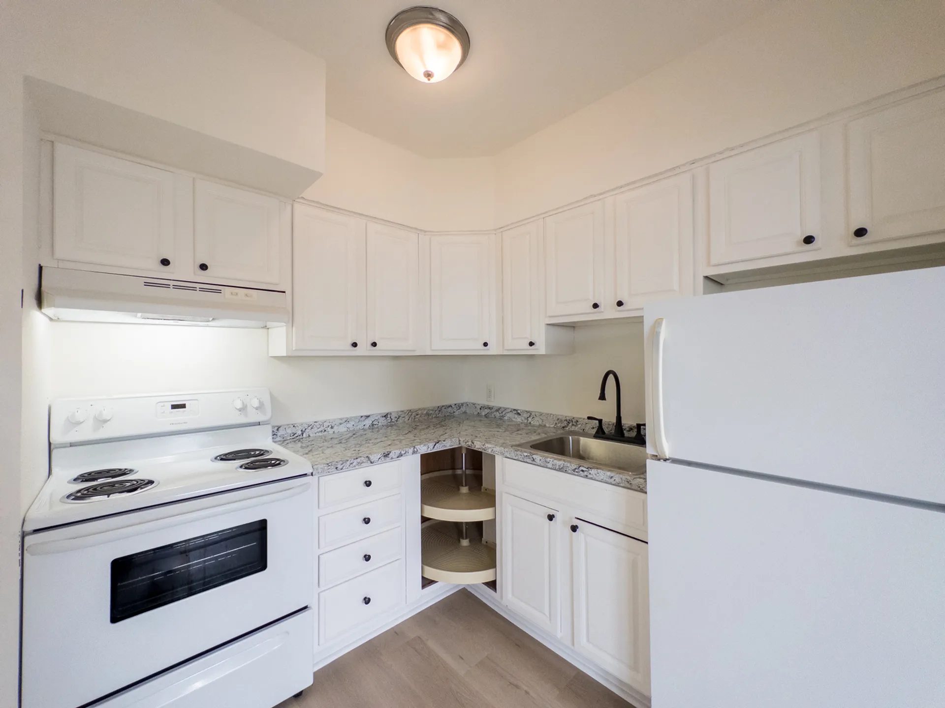 renovated apartment kitchen, refrigerator, range with hood, lots of cabinets, lazy susan cabinet storage, stone countertops, modern sink, overhead light