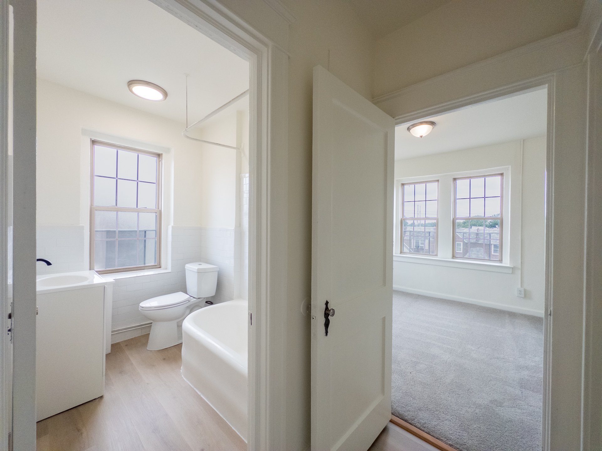 view from hallway into bathroom and bedroom, big windows, overhead lights, carpet, wood floor