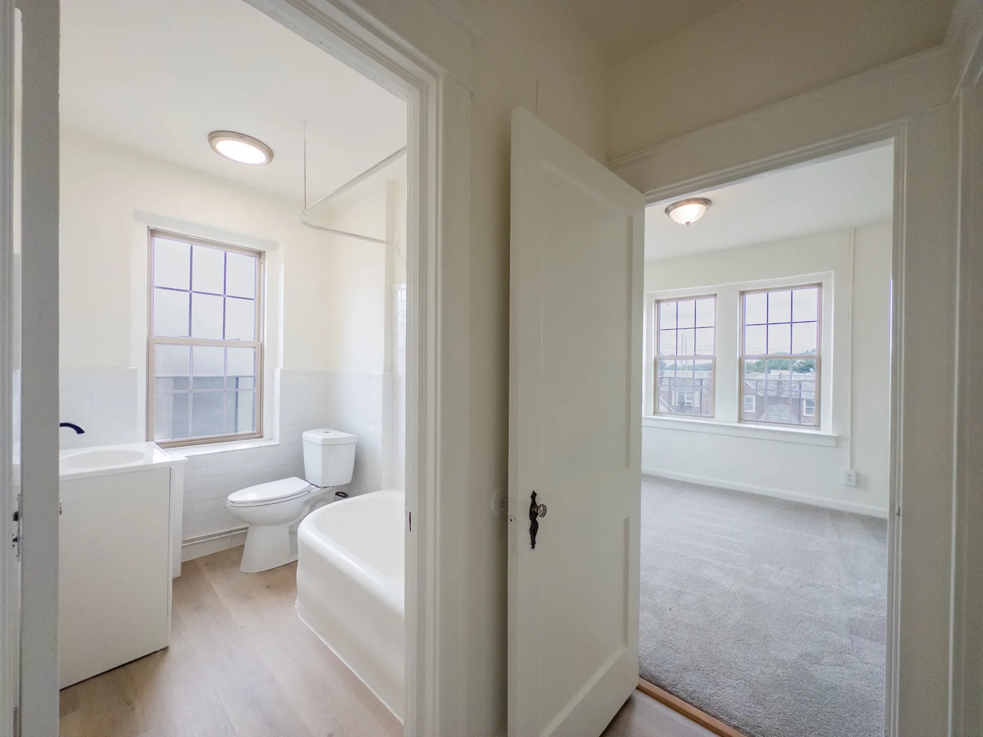 view from hallway into bathroom and bedroom, big windows, overhead lights, carpet, wood floor