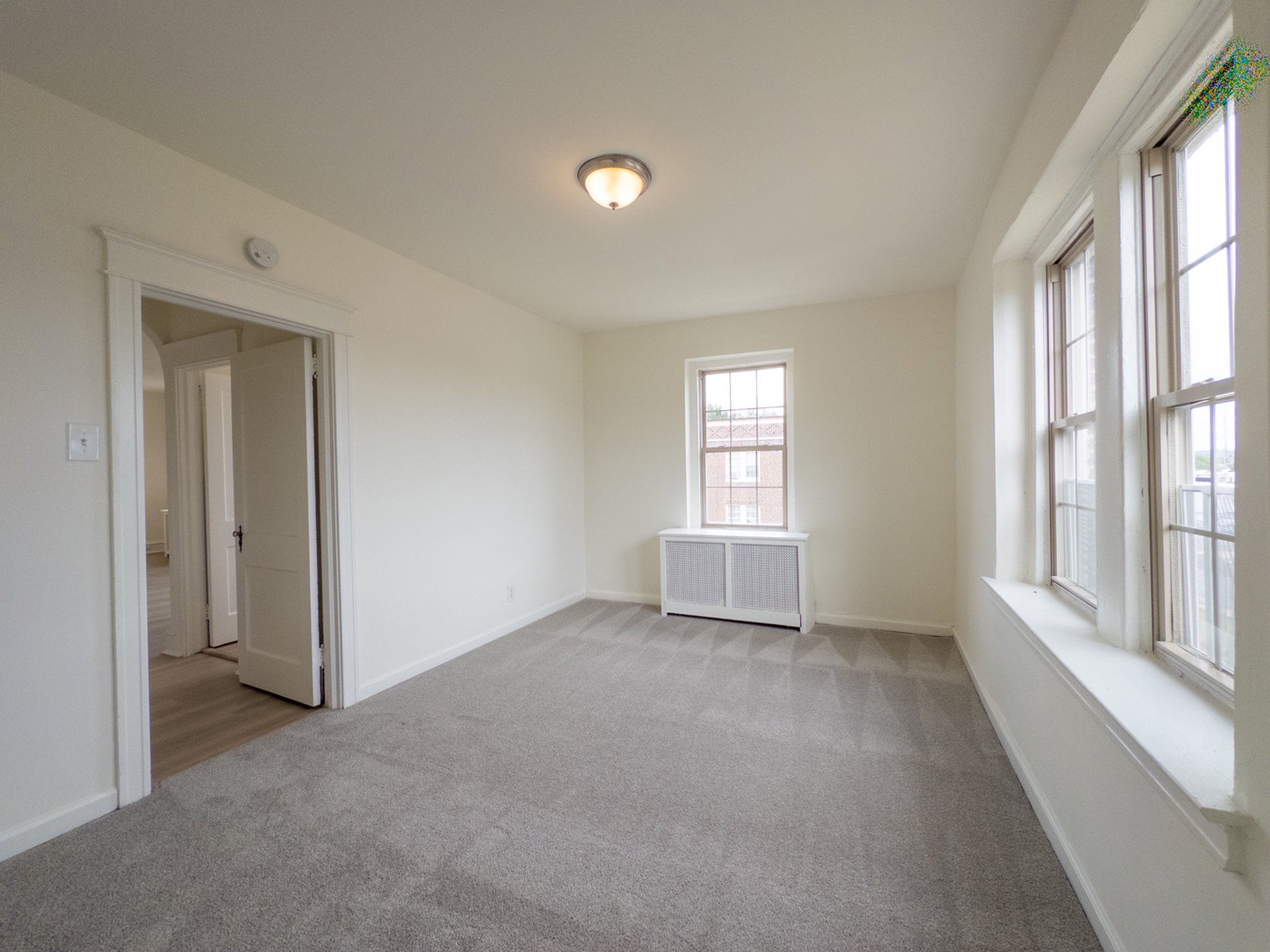 carpeted bedroom with lots of windows, closet, overhead light, radiator heat, door leading to hallway