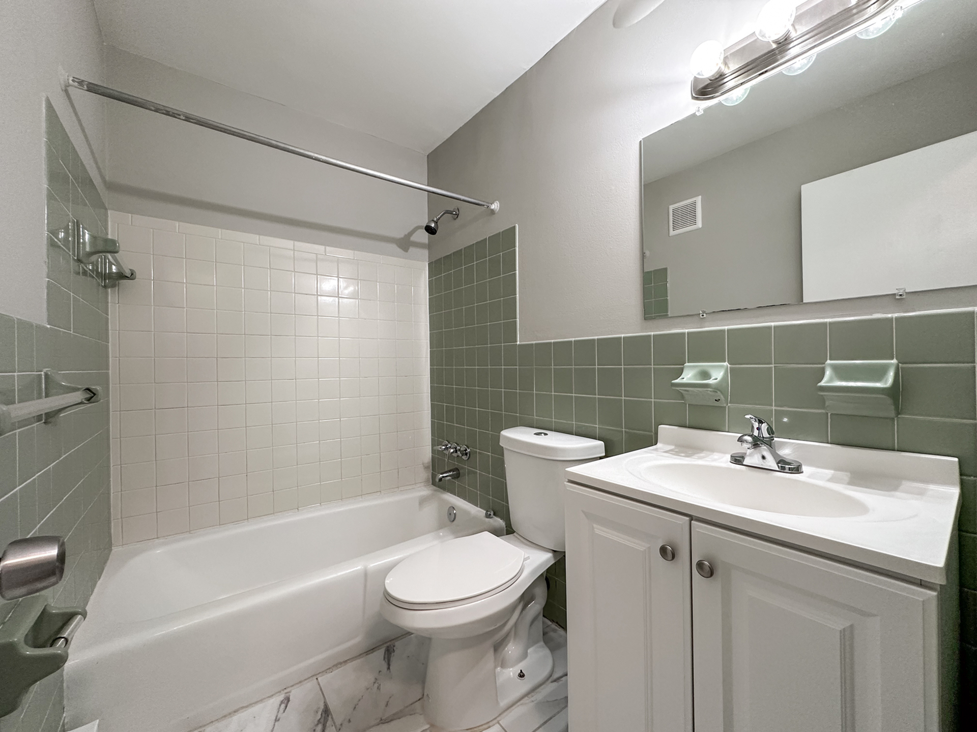 bathroom with tiled wall and shower, vanity sink, energy efficient toilet, steel accents