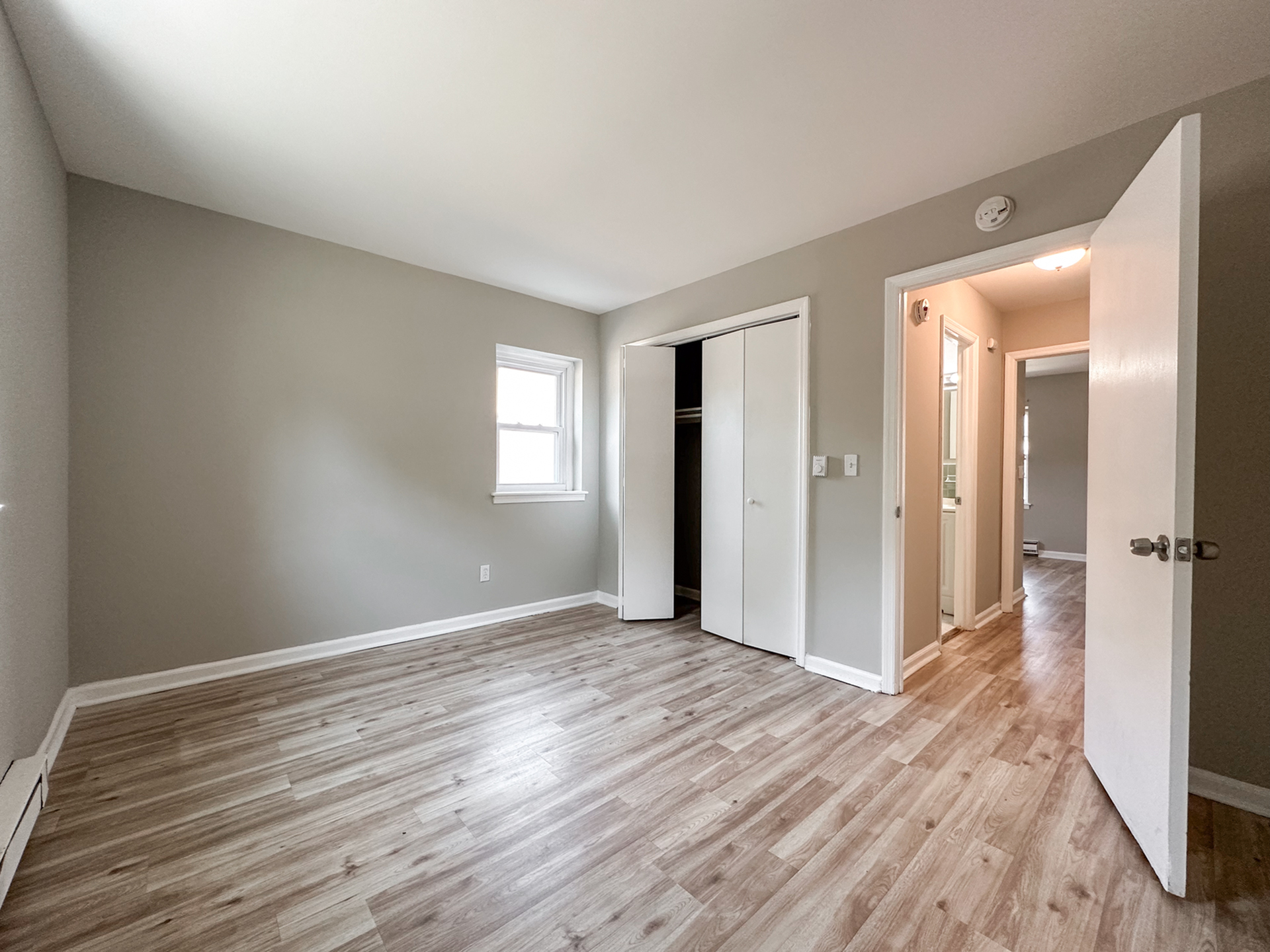 bedroom with wood panel floors, door leading to hallway, window, long closet with sliding doors