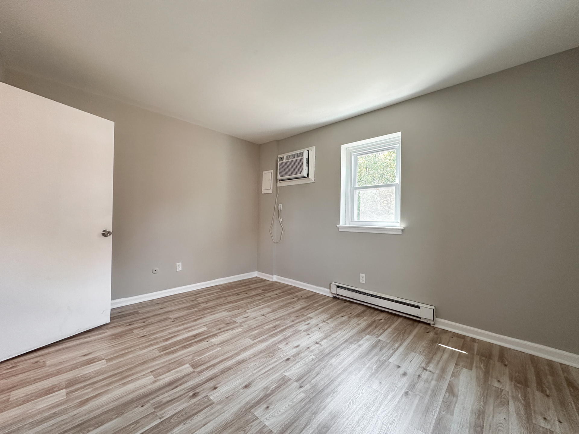 bedroom with window, air conditioner, baseboard heating, wood floor