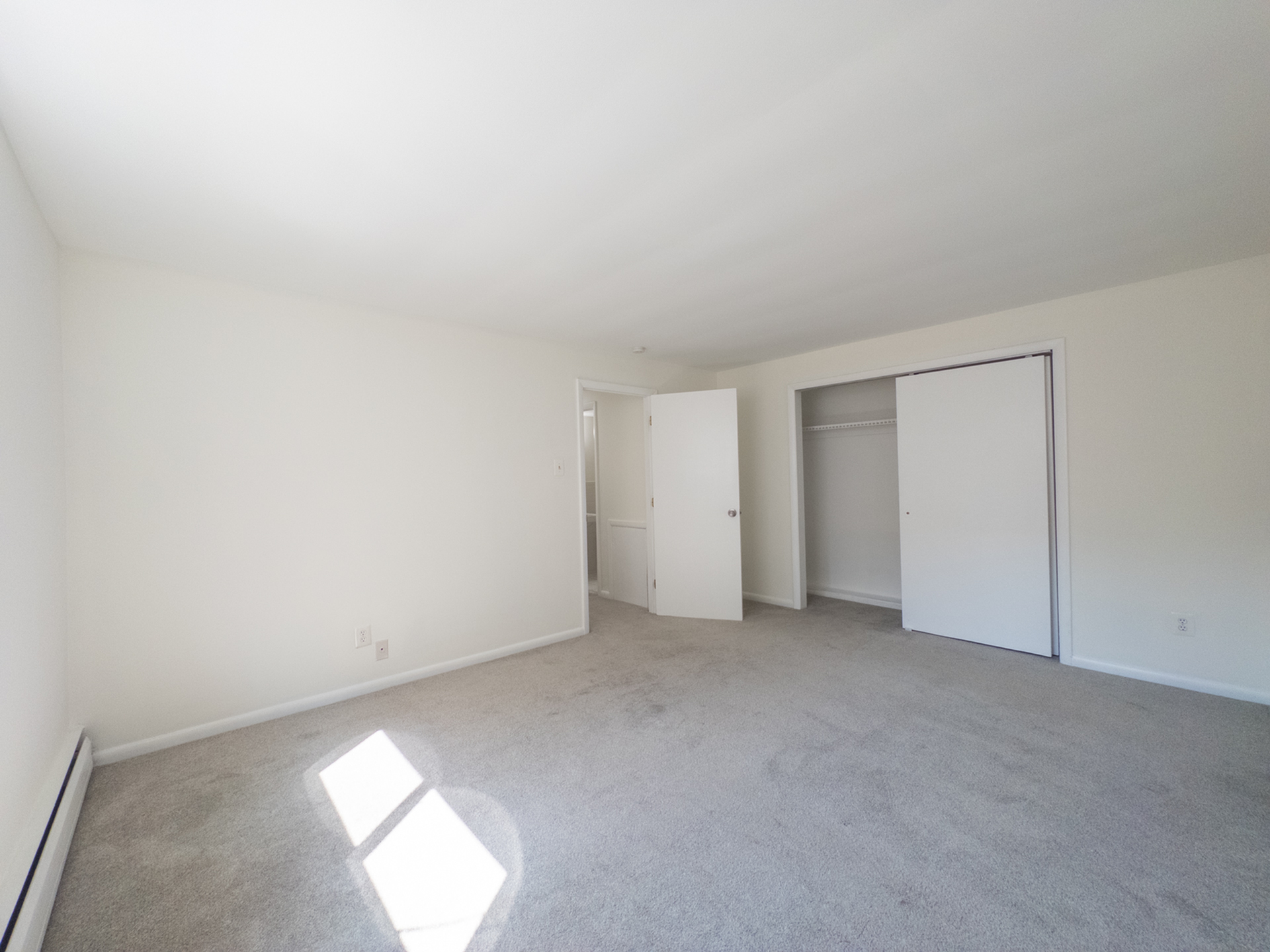 carpeted bedroom with long closet, door leading to hallway, natural light