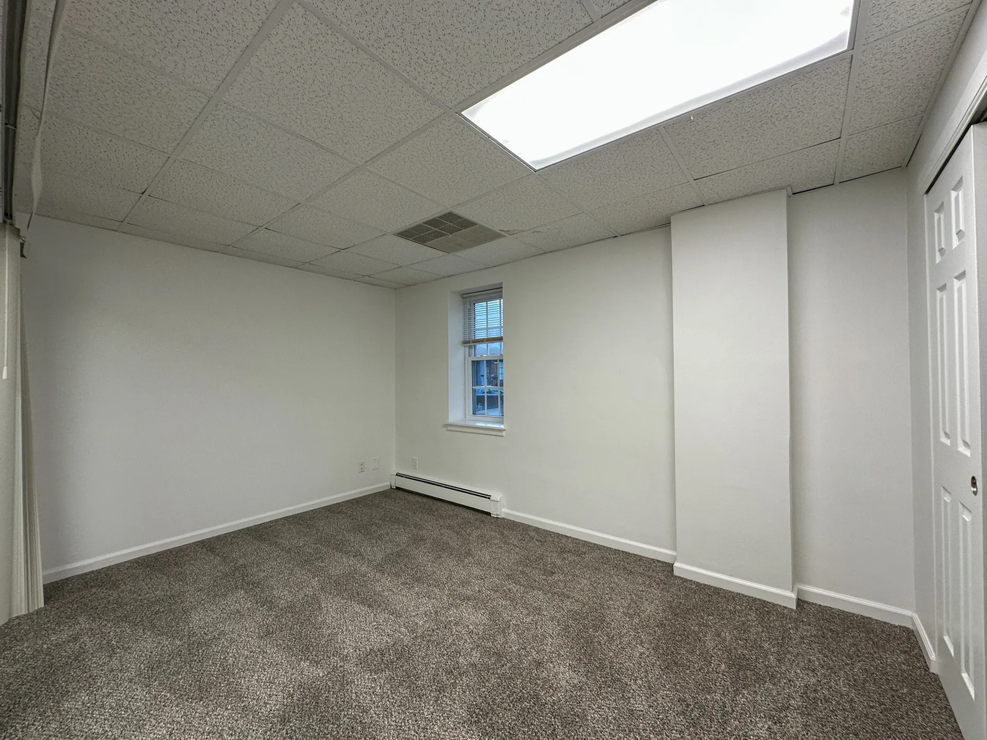 Bright and spacious room with fresh carpeting, featuring a large window and clean white walls, ideal for a cozy bedroom or office space.