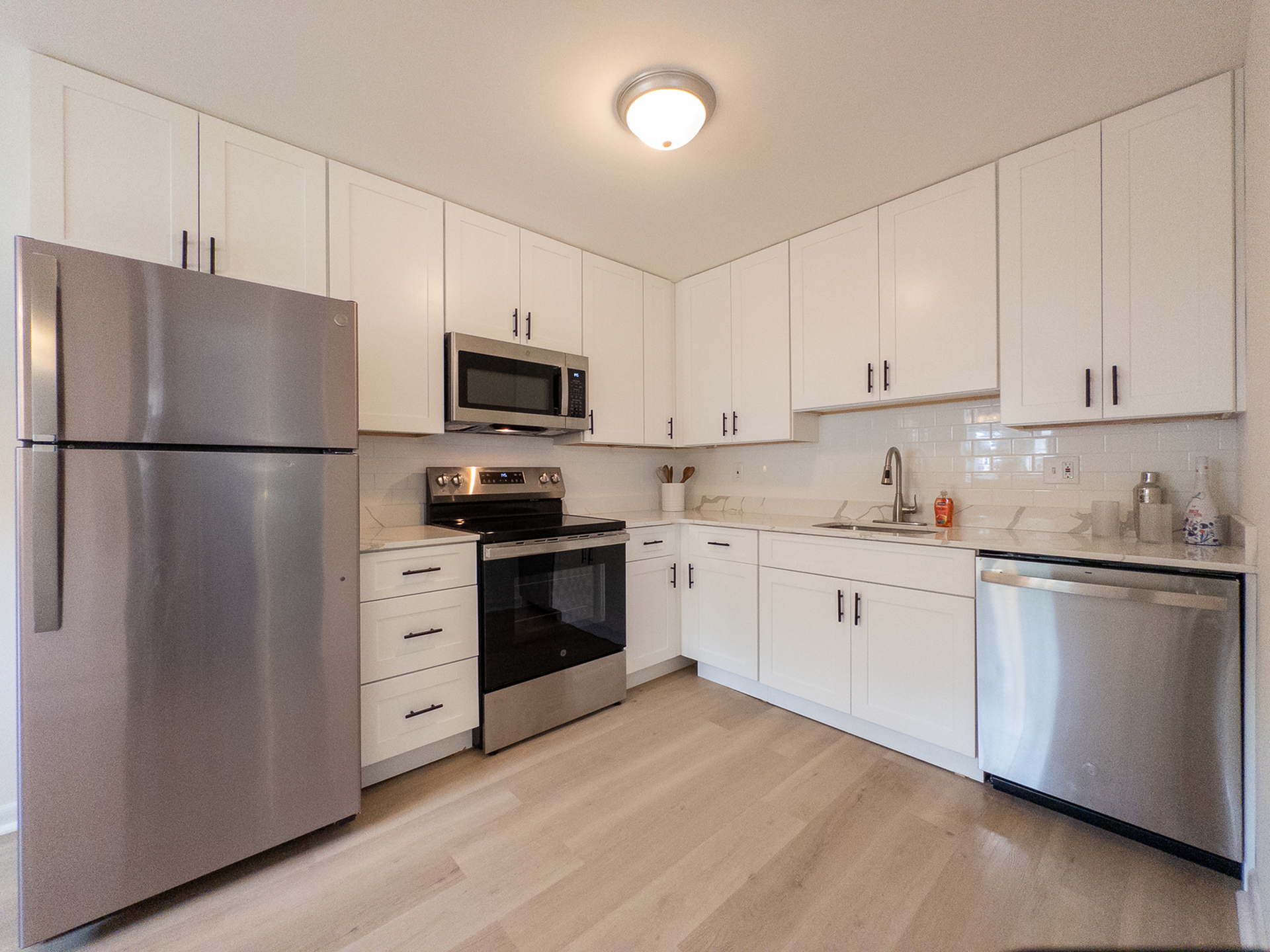 Modern kitchen with sleek stainless steel appliances, elegant white cabinetry, and stylish light wood flooring.