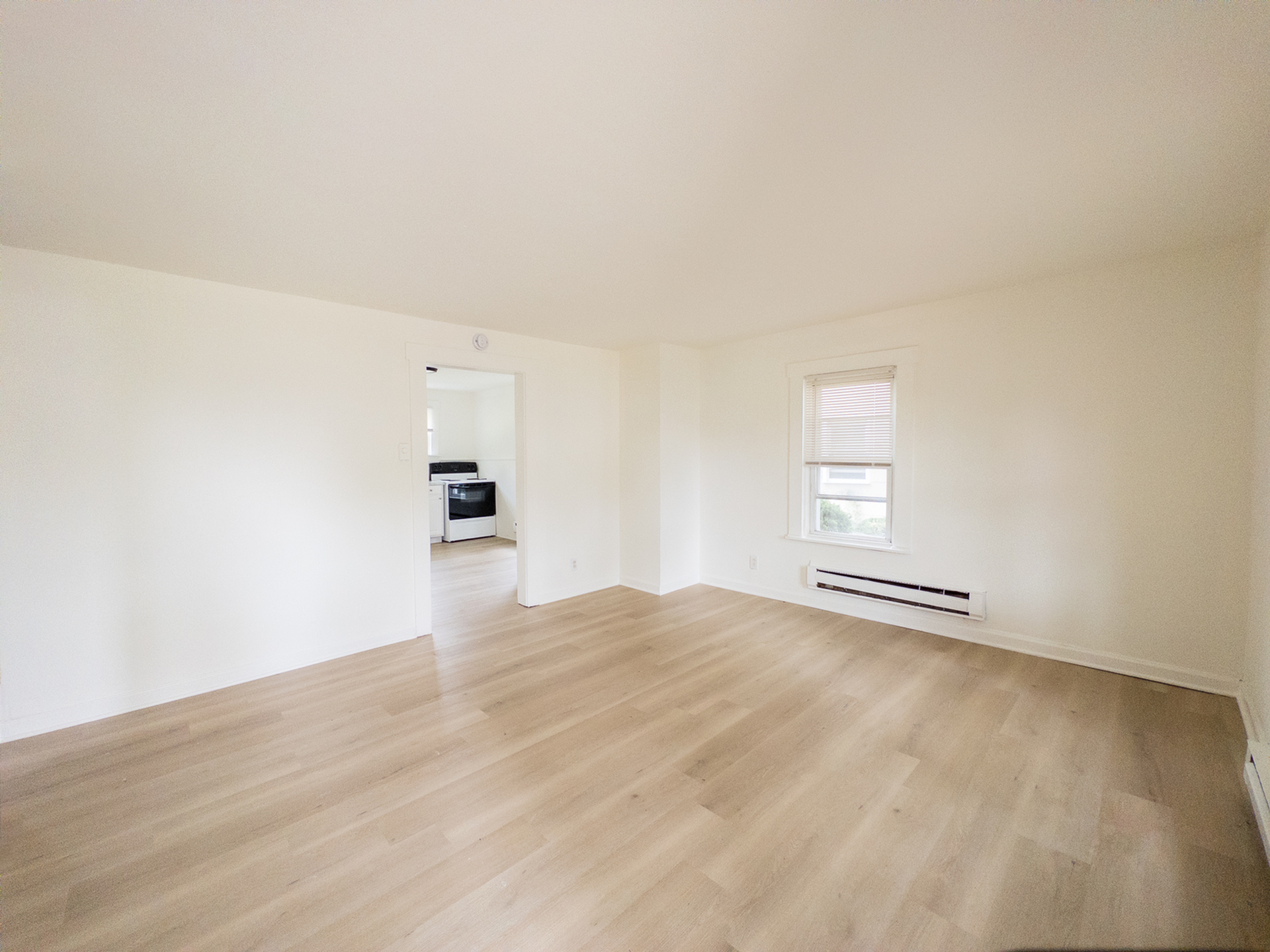 Bright and airy living room with elegant wood flooring, showcasing an open doorway to a modern kitchen.