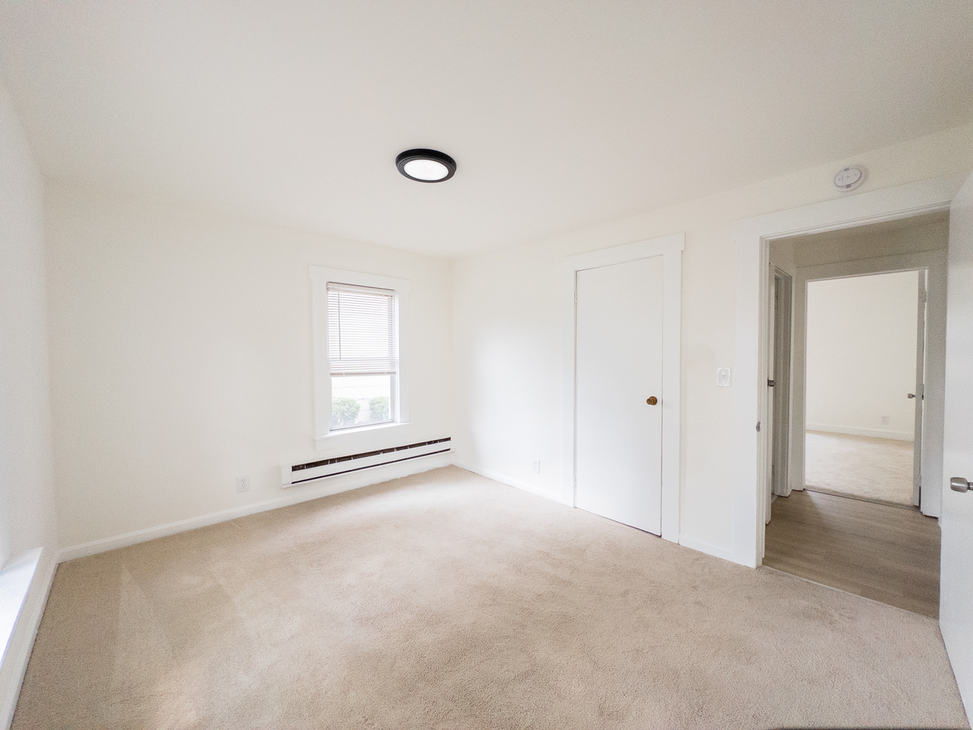 Bright and airy bedroom with plush carpeting, large window, and neutral walls, offering a peaceful retreat.