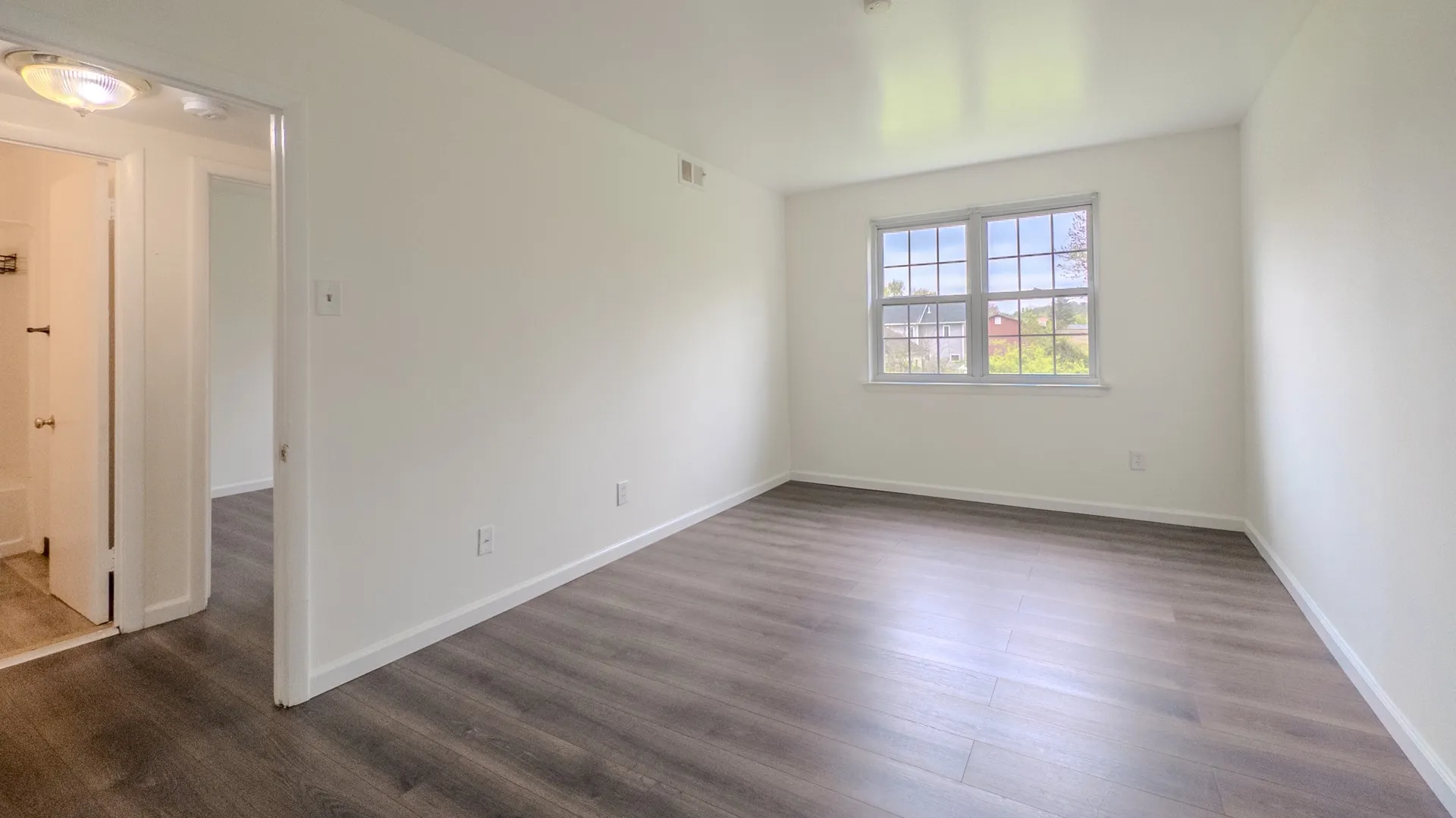 bedroom with plank flooring and a large window, doorway on the left leading to hallway