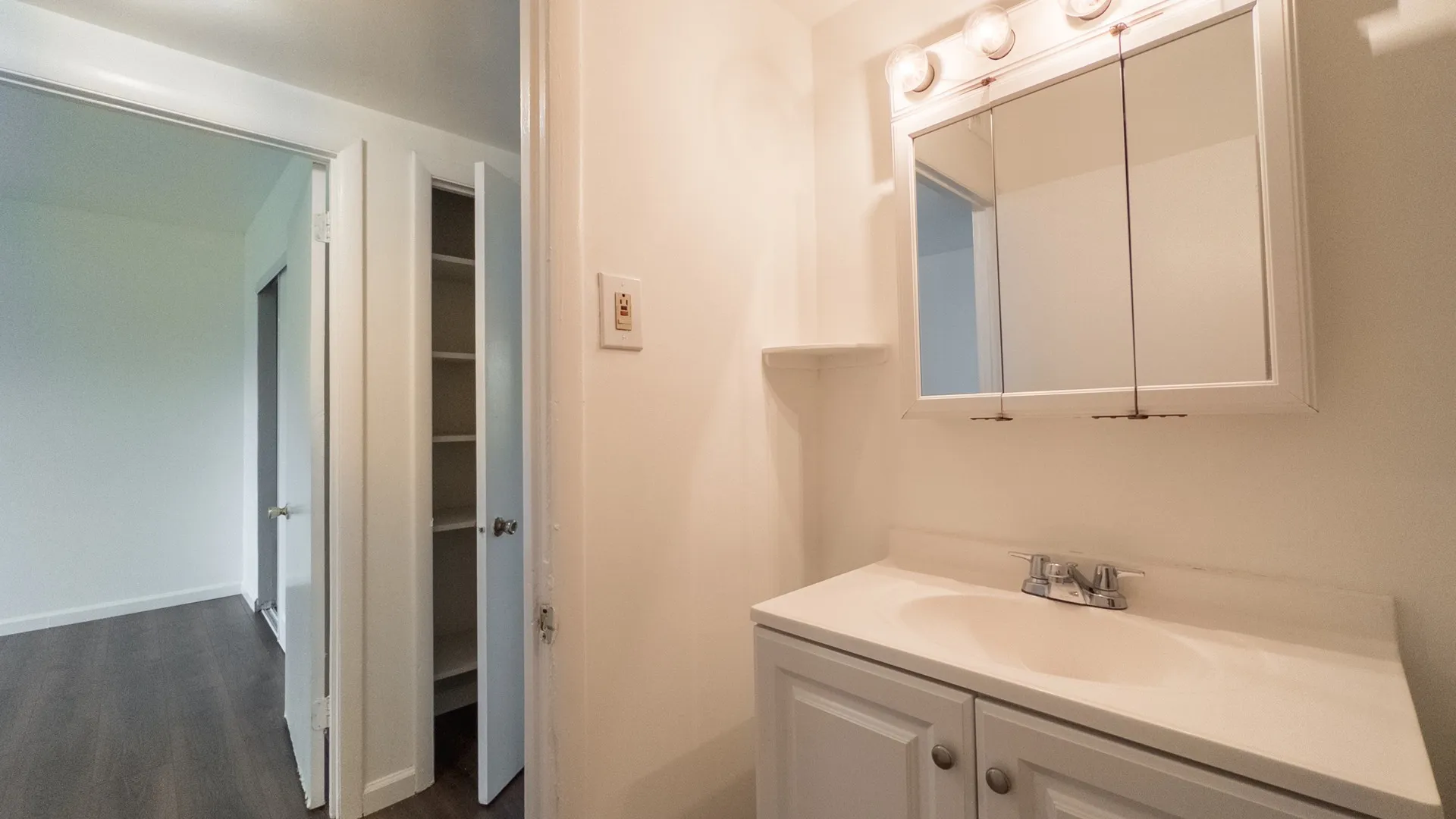 bright bathroom with vanity sink, hallway leading to bedroom, linen closet