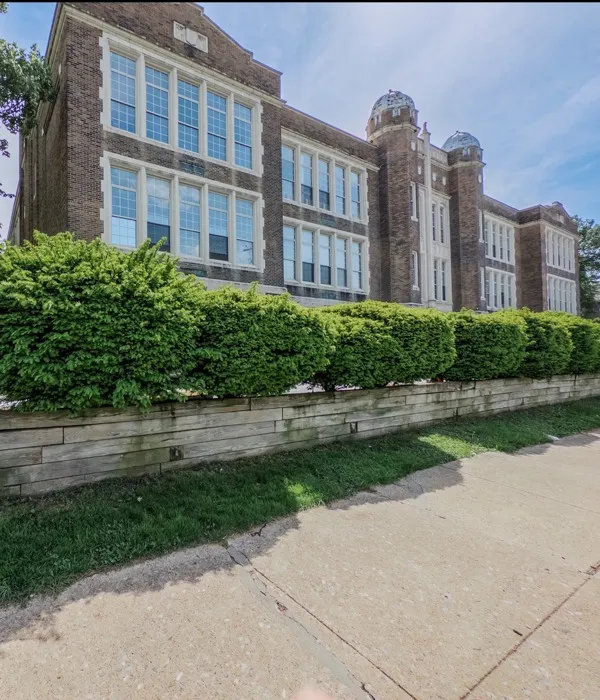 large school building, apartment sign, green hedges in raised beds along sidewalk