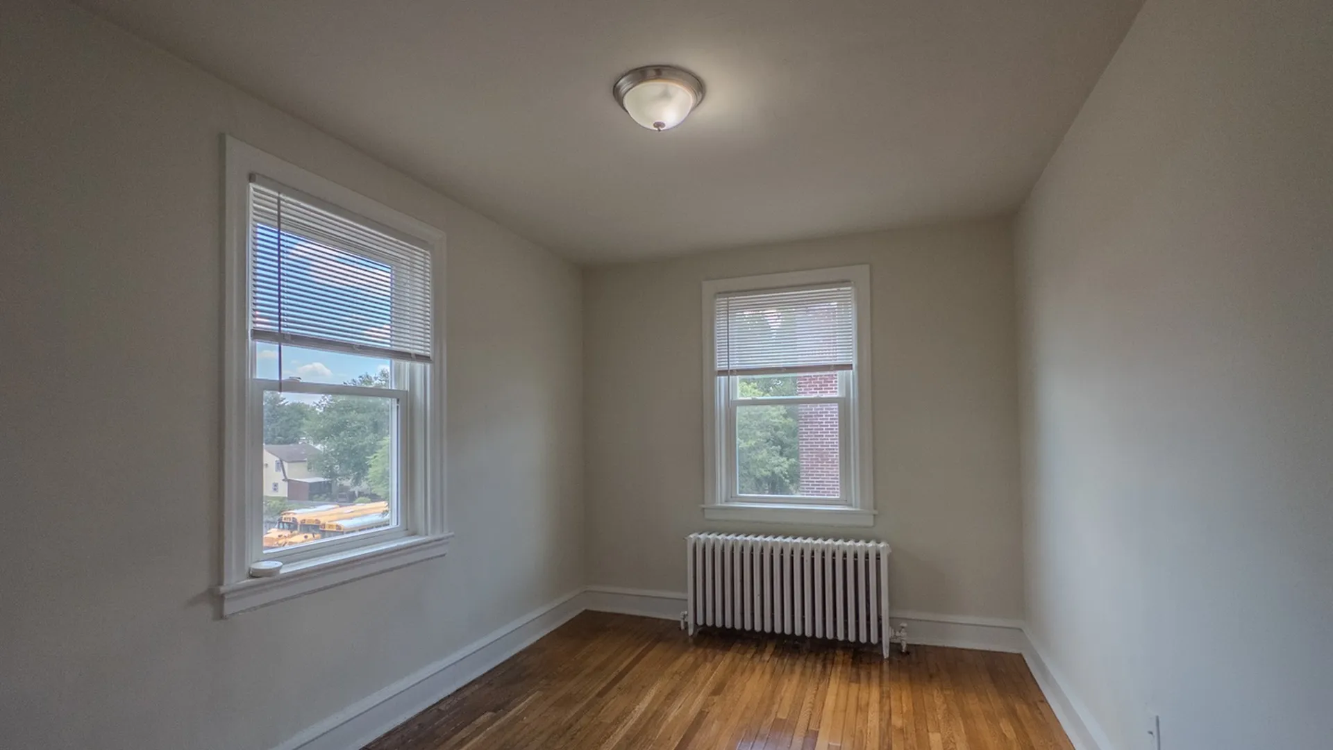 apartment bedroom looking out large windows, radiator and overhead light