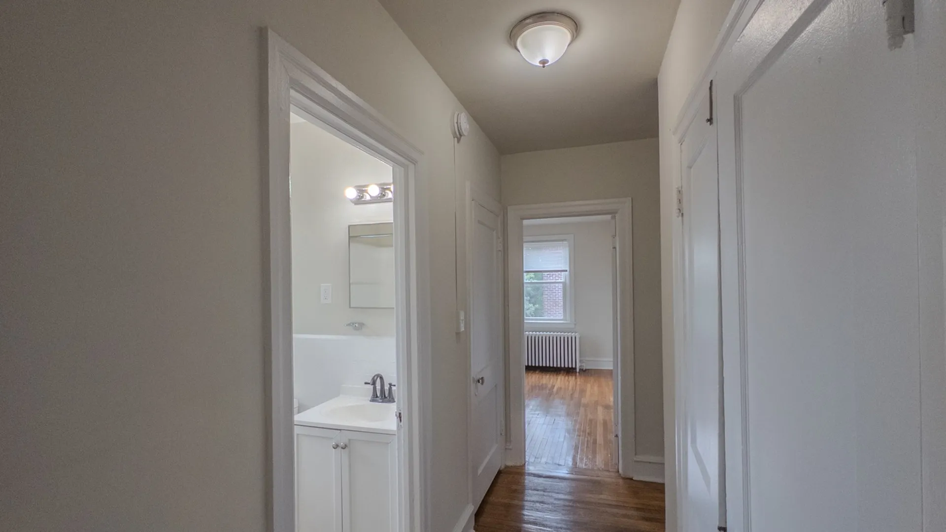 view down apartment hallway passing closet and bright bathroom, leading into bedroom