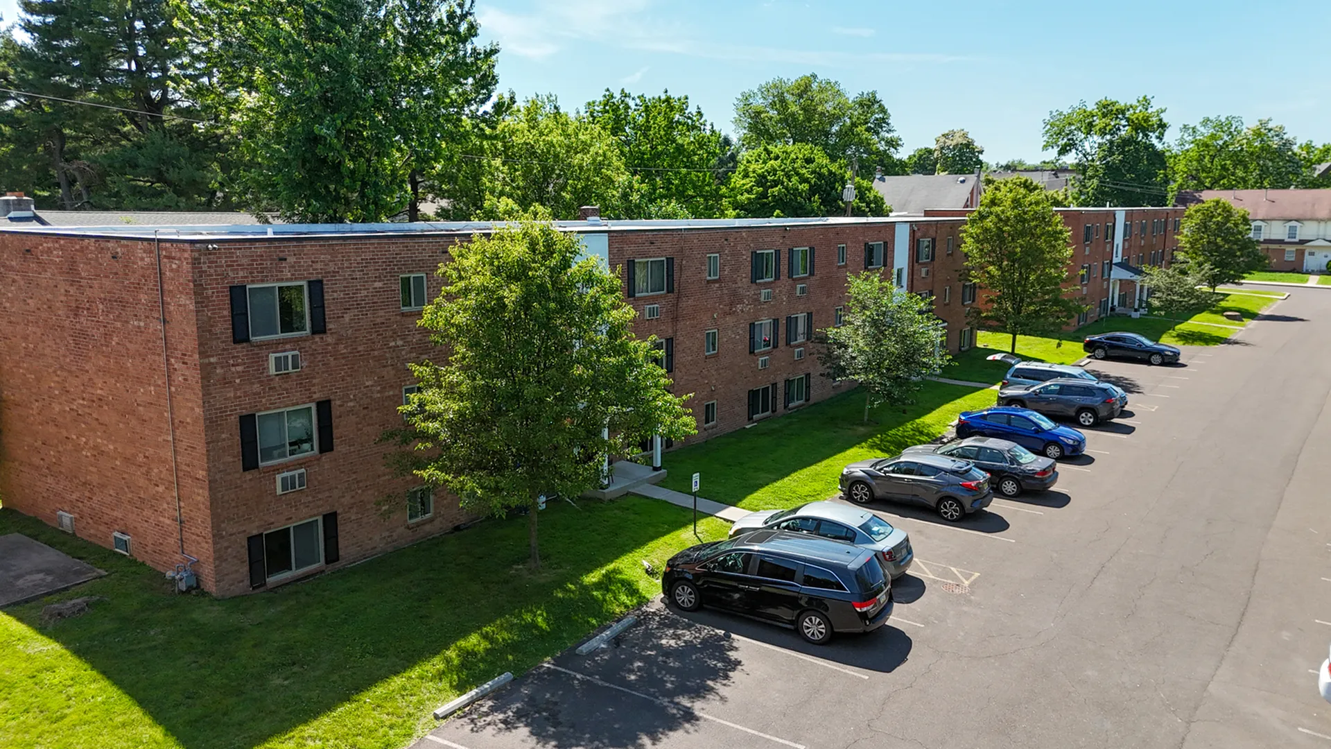 brick apartment building surrounded by grass and lined with trees