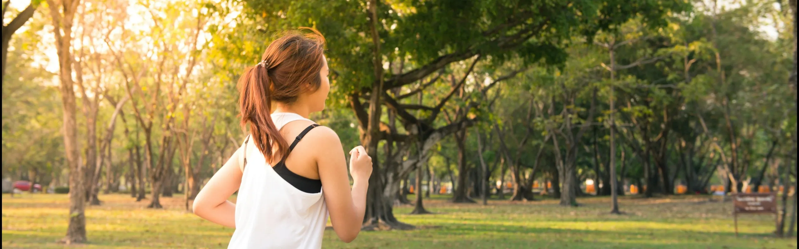 girl jogging in park, sunny, surrounded by trees