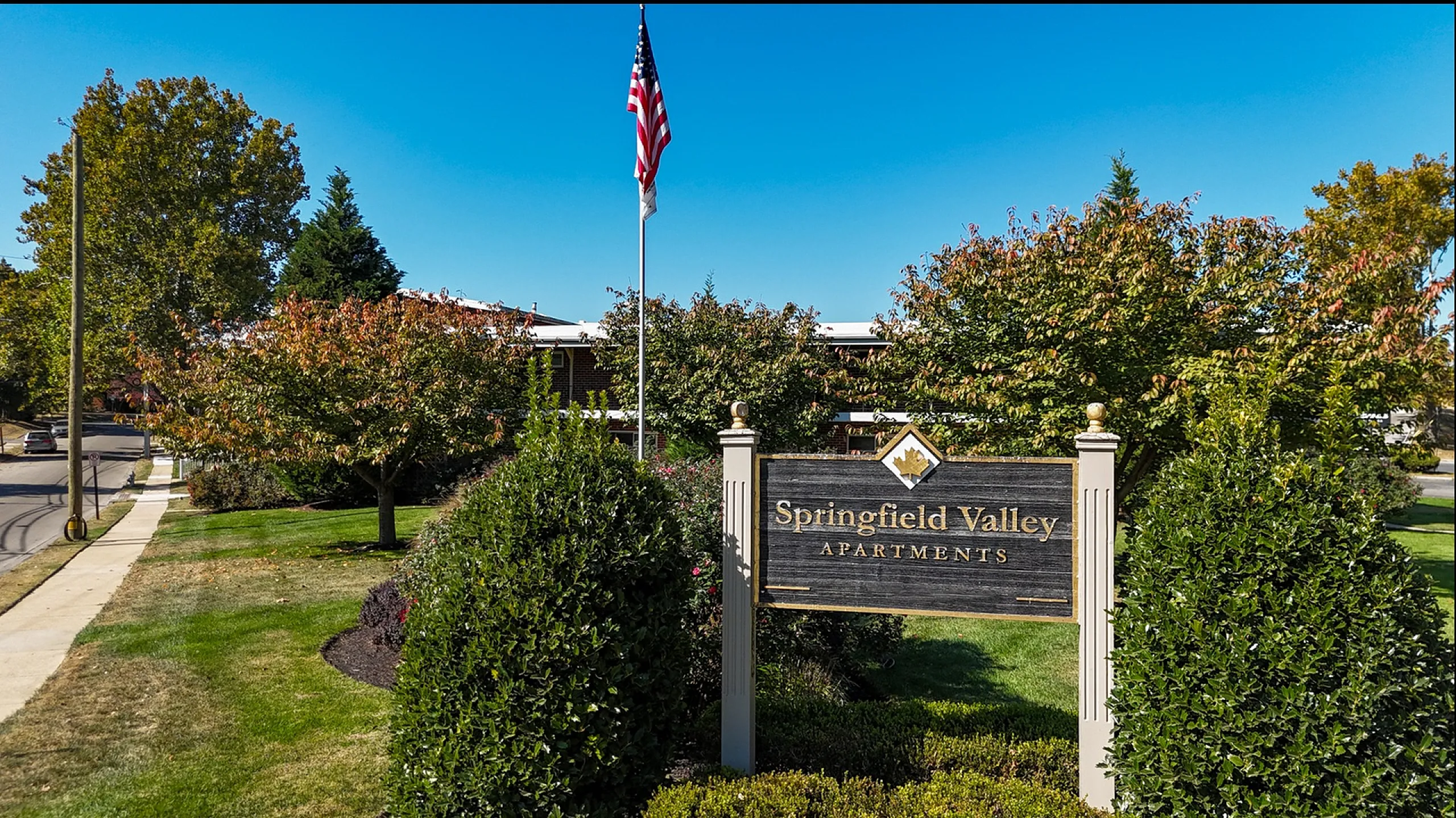exterior view of springfield valley apartments, brick building with manicured grass, sign in beautiful flower bed, blue sky, concrete walkways