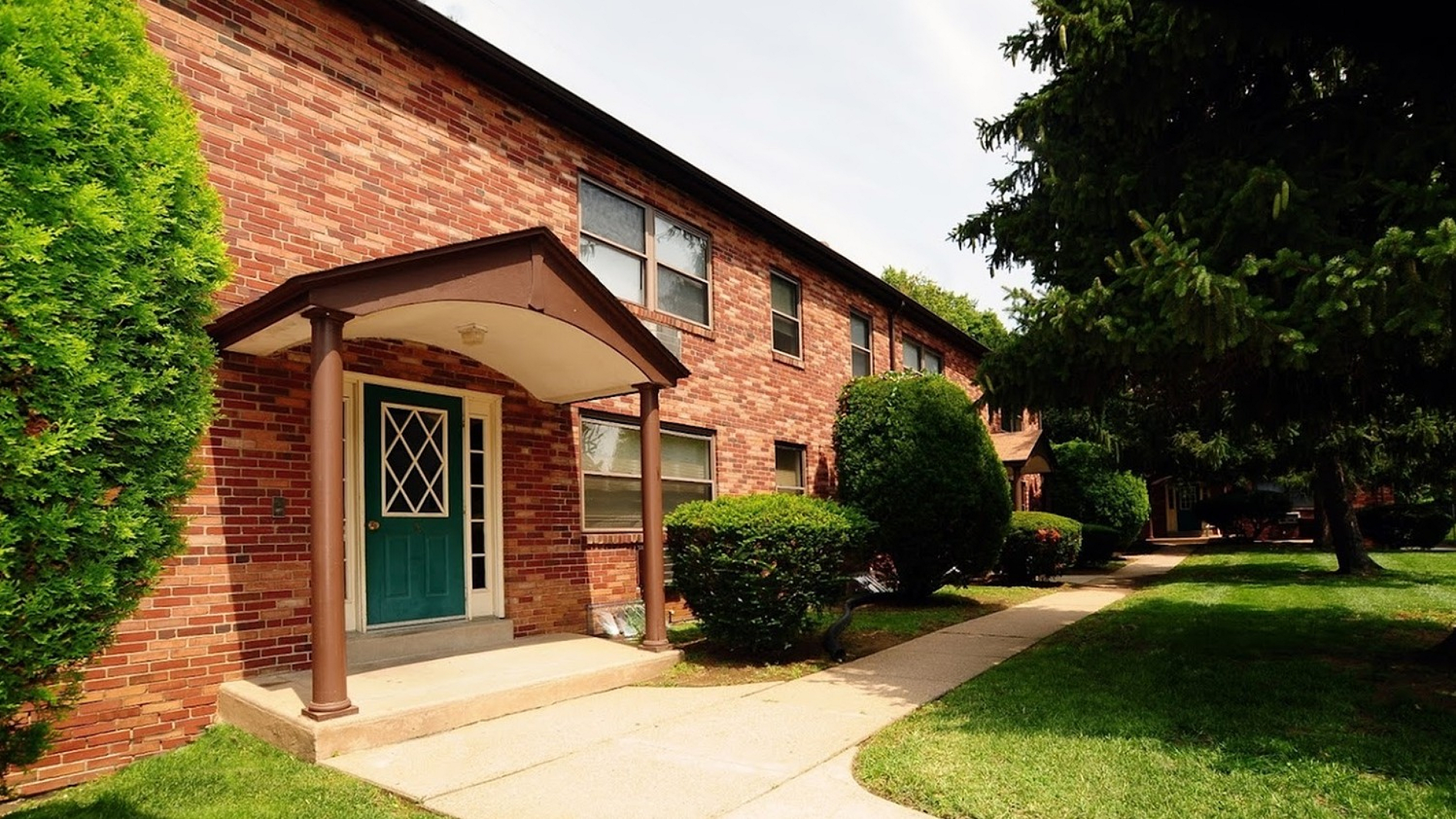 Inviting brick apartment building with lush green landscaping and a welcoming entrance with a green door.
