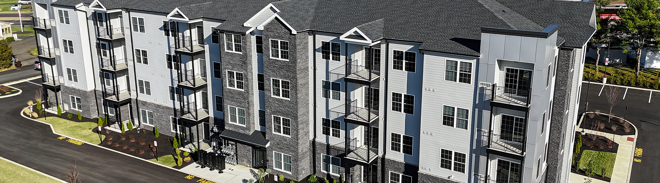 Modern apartment building with stylish architectural design featuring multiple balconies, set amidst lush greenery and a well-maintained landscape.