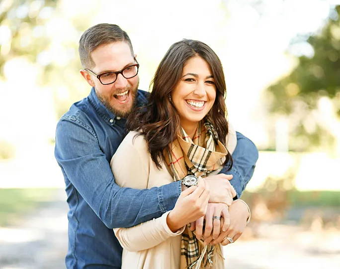 Joyful couple embracing outdoors, surrounded by lush greenery, exuding warmth and happiness.