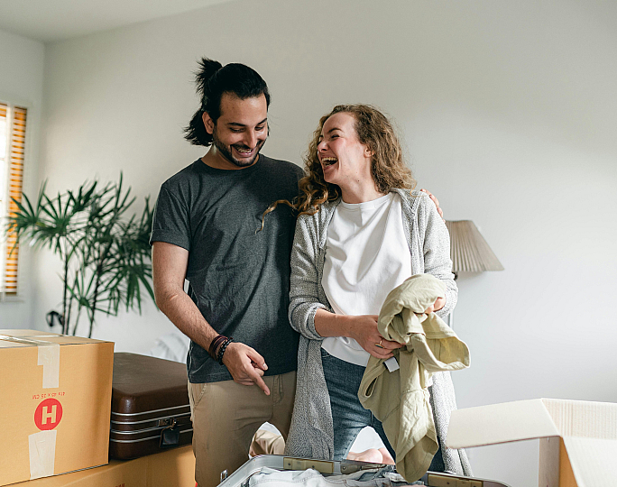 Happy couple unpacking boxes in a brightly lit room, ready to settle into their new home.