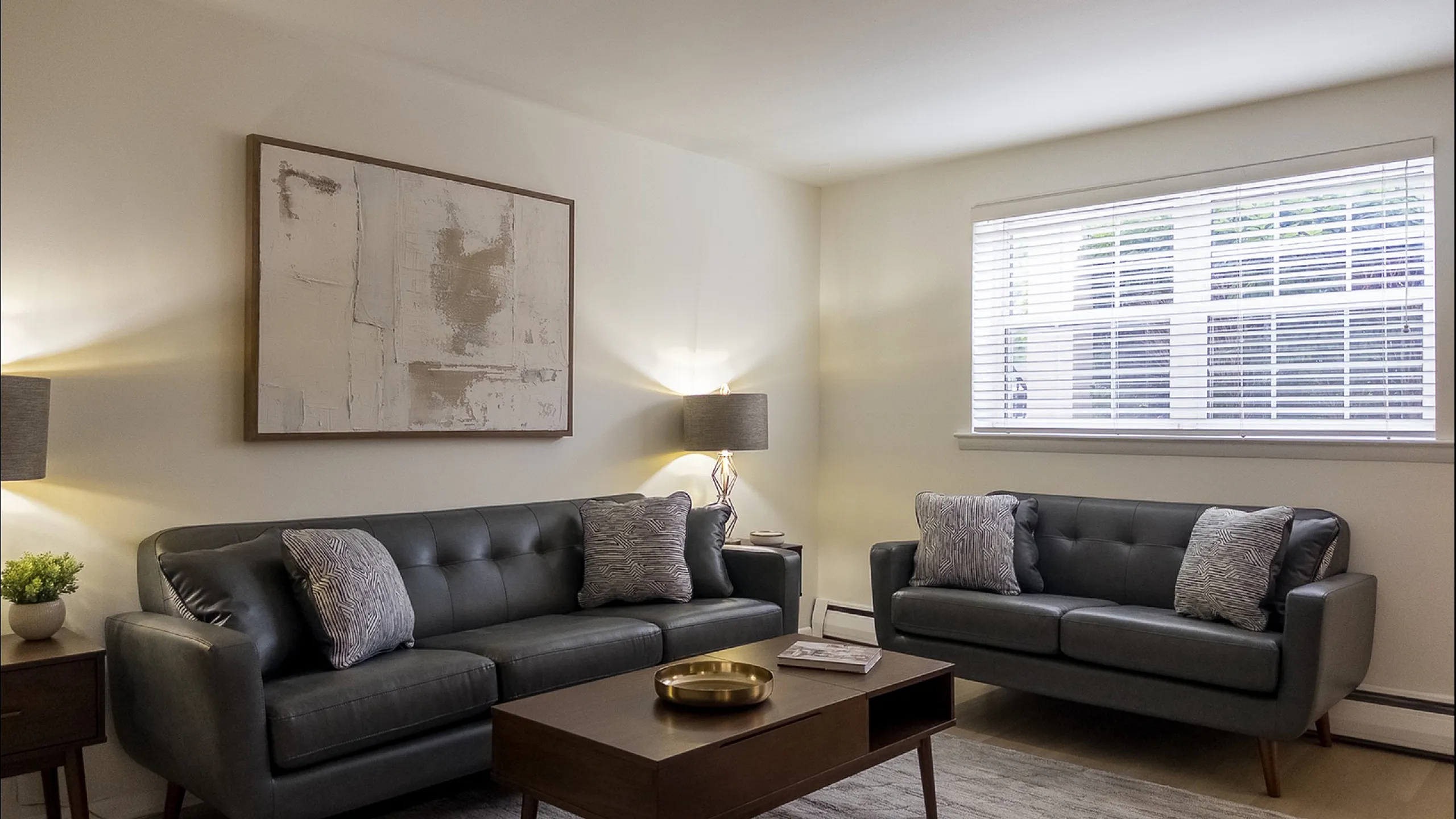 Elegant living room with stylish grey sofas, modern art, and abundant natural light from large windows.