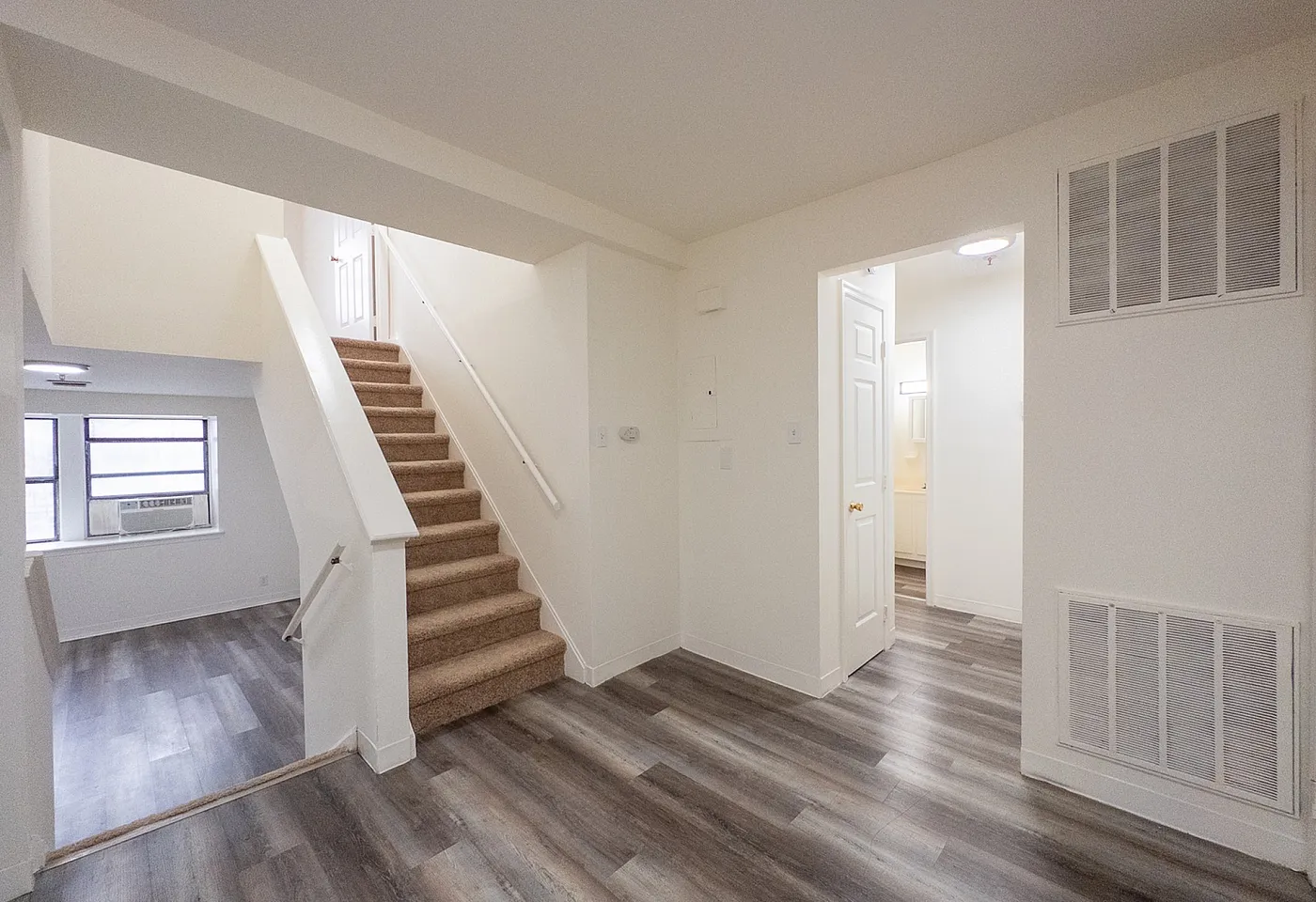 Bright, open hallway with modern laminate flooring, leading to a cozy carpeted staircase and newly renovated interiors.