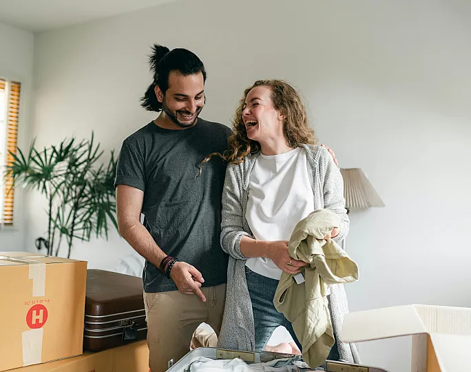 Happy couple unpacking boxes in a bright, modern living space with natural light and stylish decor.