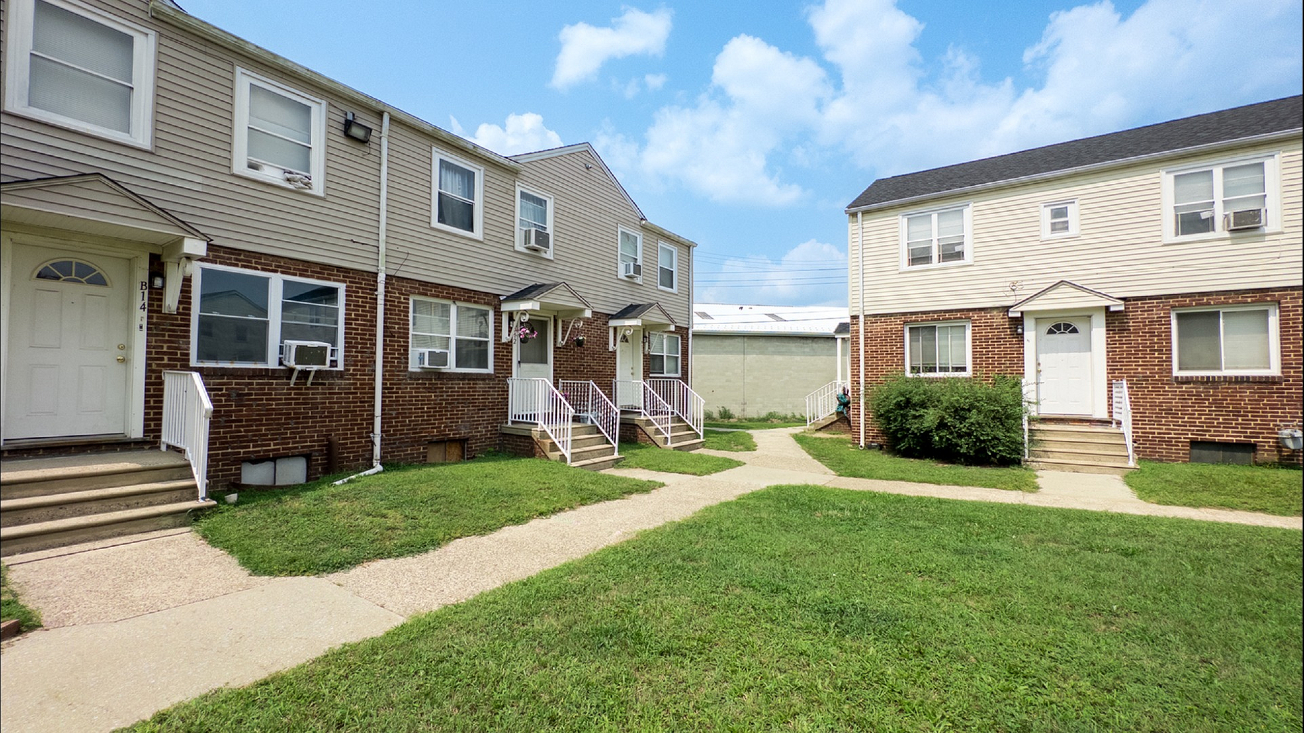 Charming brick townhouse community with inviting entryways and well-maintained lawns under a bright blue sky.