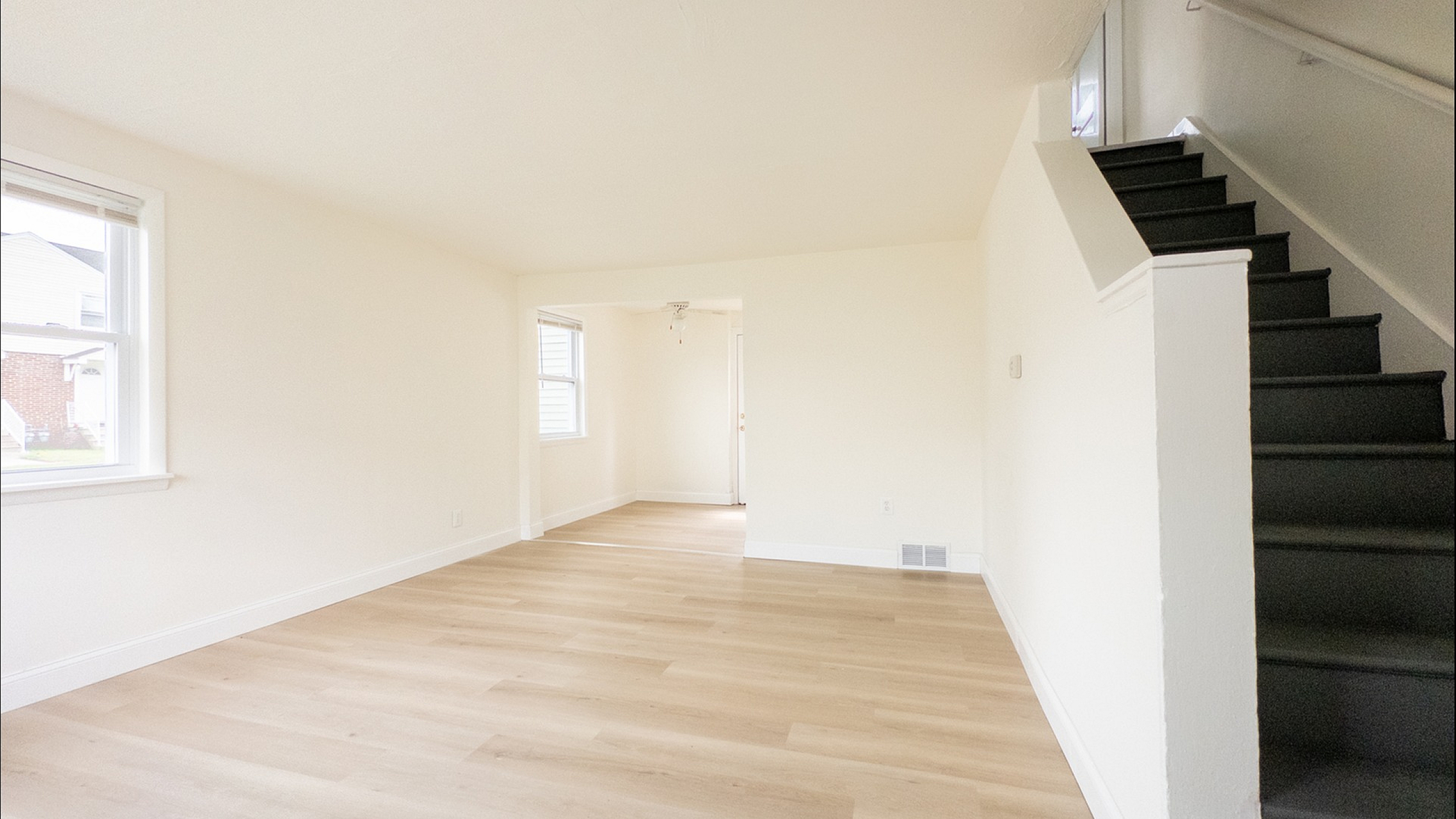 Bright and airy open-plan living space with elegant wood flooring and a modern staircase, perfect for stylish urban living.