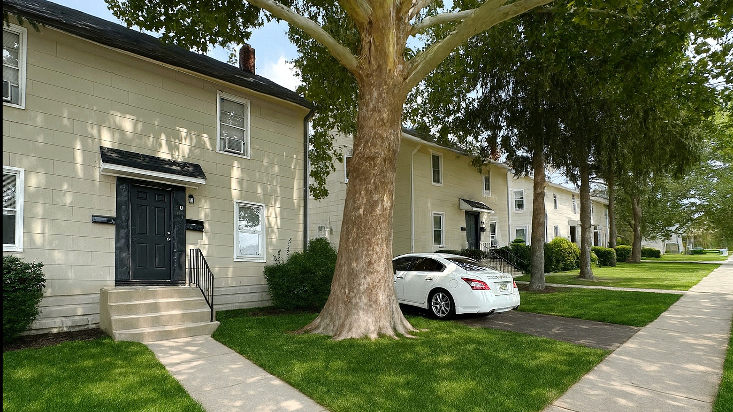 Charming apartment complex with well-maintained lawns, vibrant greenery, and ample parking space under mature trees.
