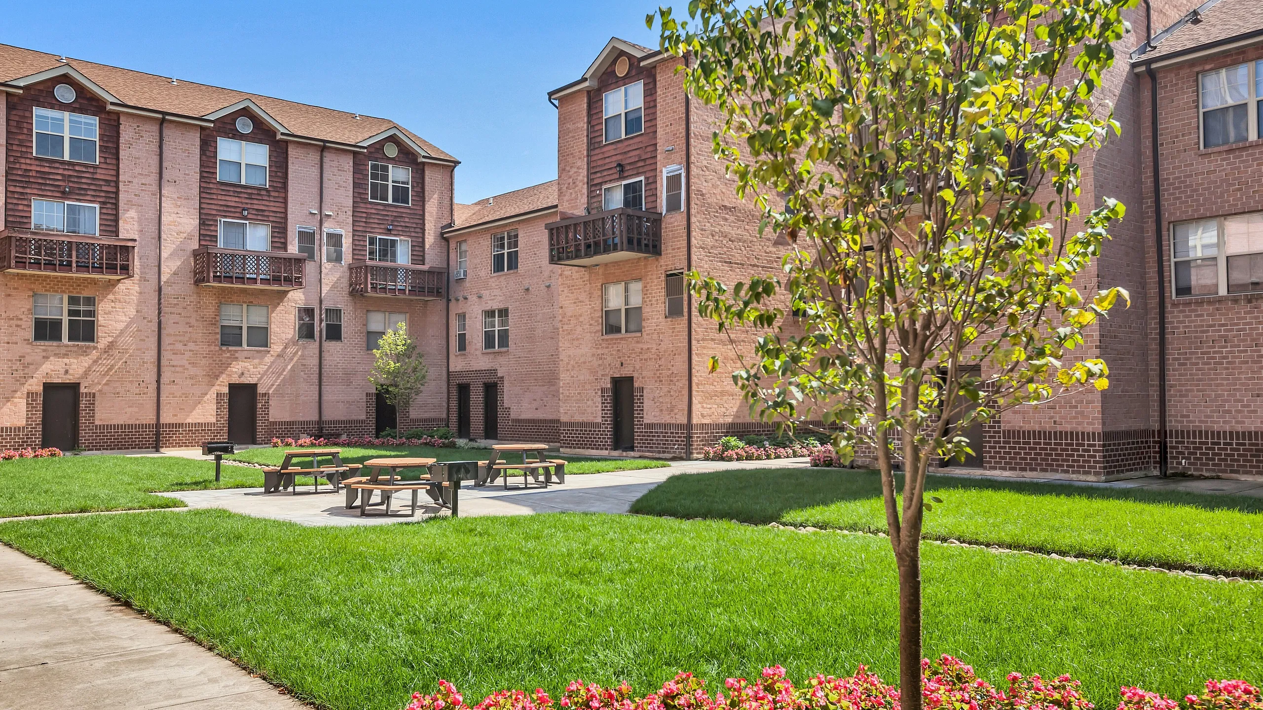 Charming apartment complex with beautiful brick exterior, lush green courtyard, and picnic area, ideal for relaxation.