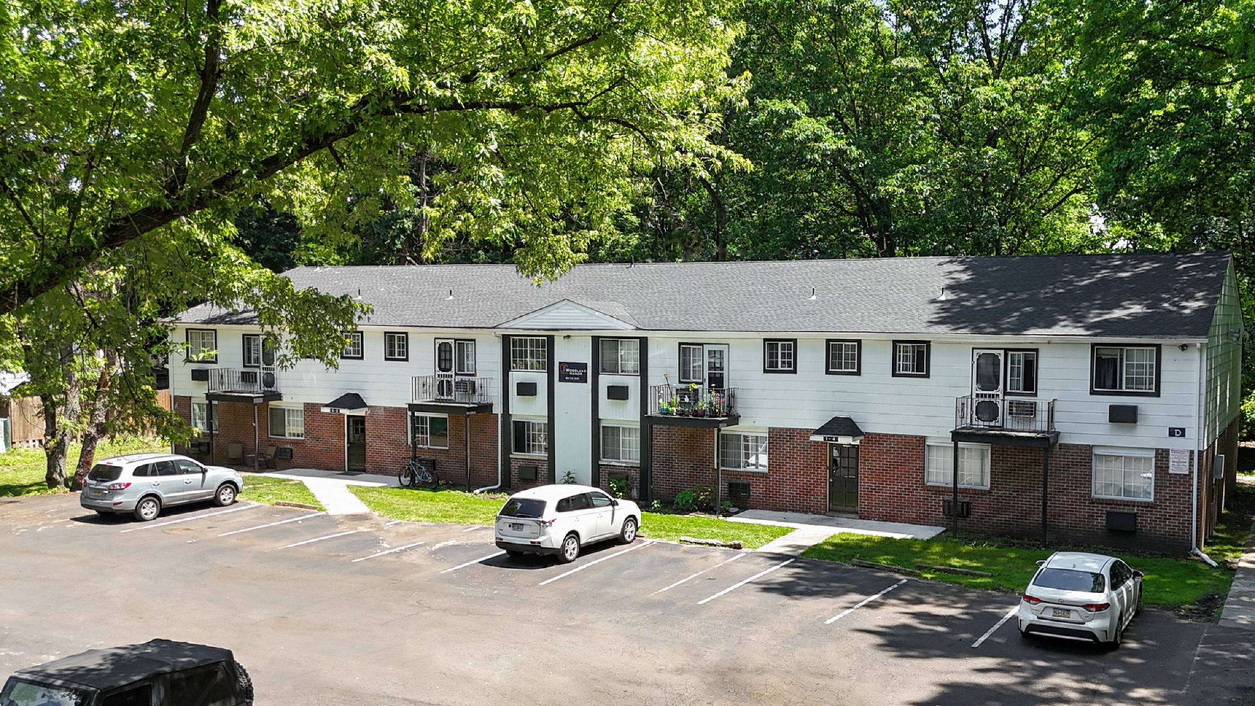 Charming apartment complex nestled among lush trees, featuring ample parking in a peaceful, green setting.