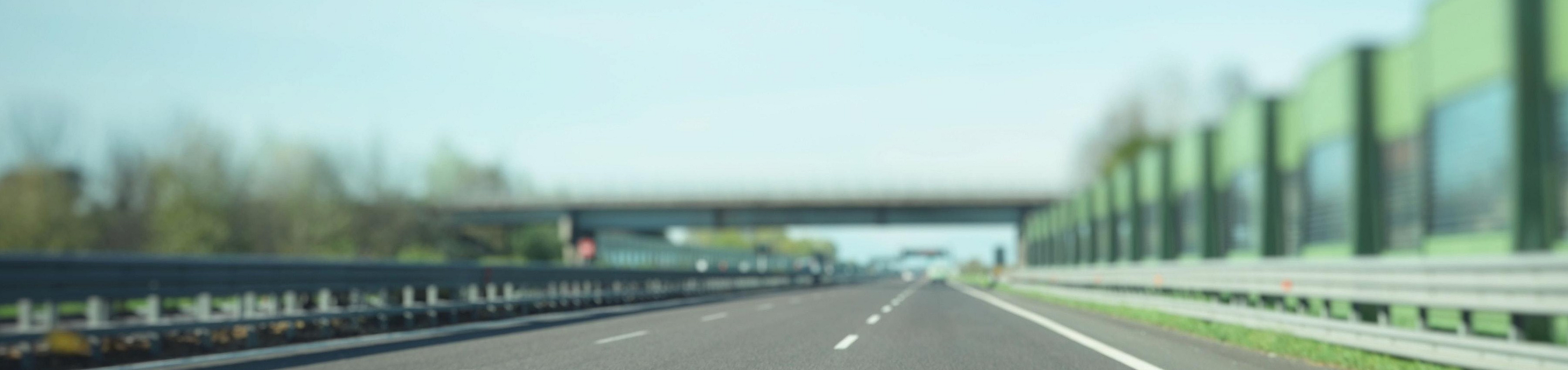 Peaceful and expansive highway view with clear blue skies, green noise barriers, and lush surroundings.